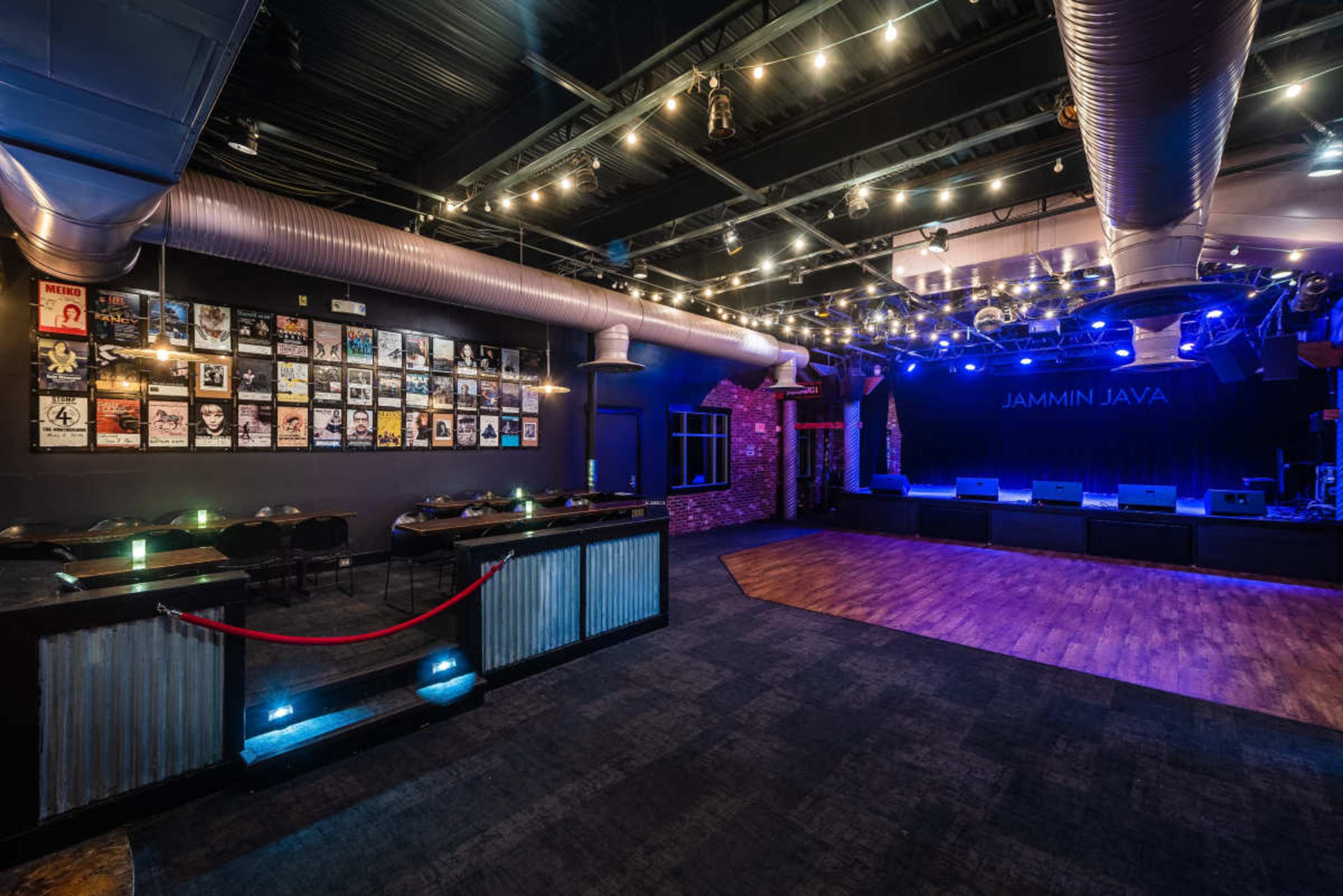 The image shows an empty music venue with a stage, seating areas, and walls adorned with framed posters.