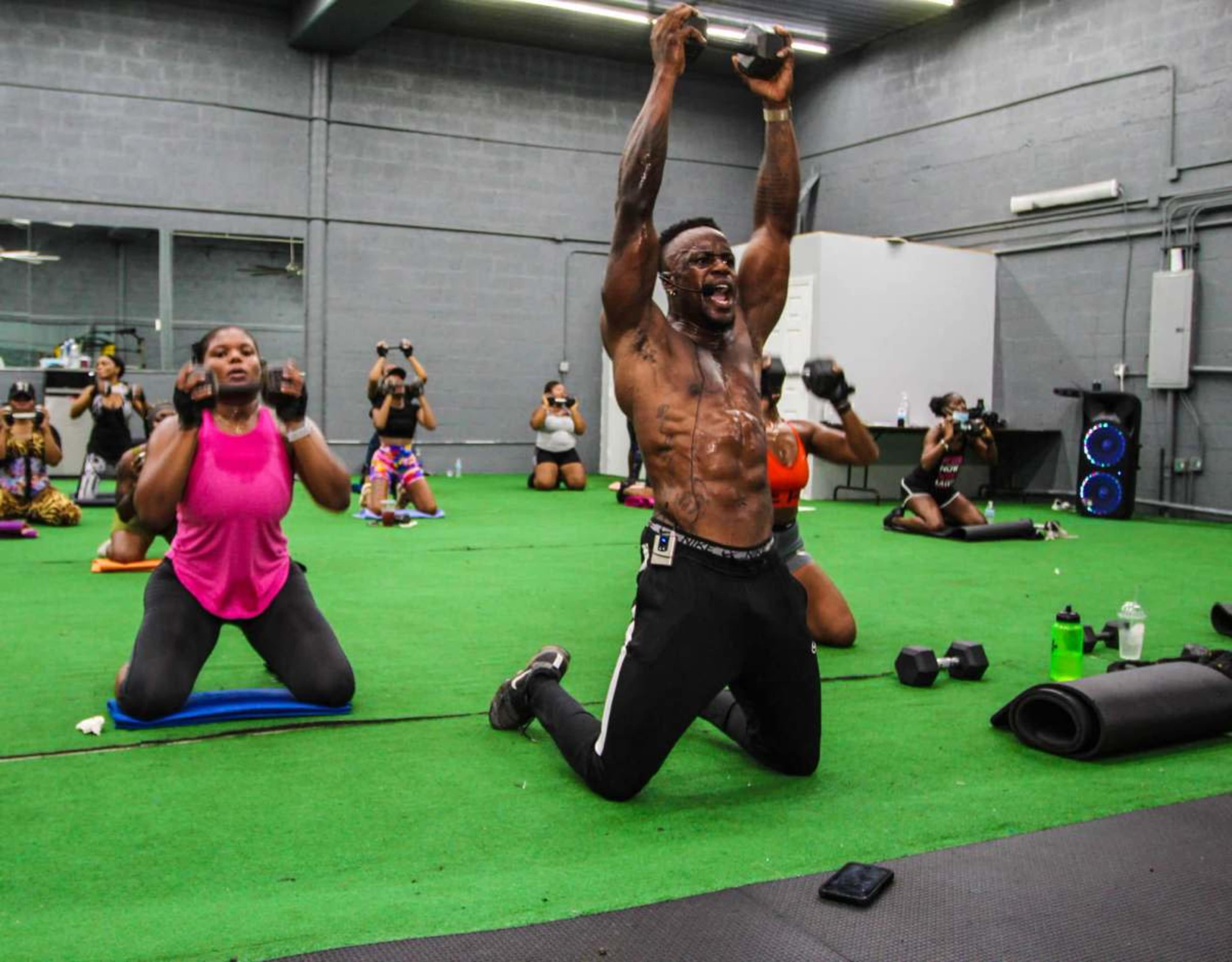 A fitness class is in session, with participants using dumbbells while on mats in a gym.