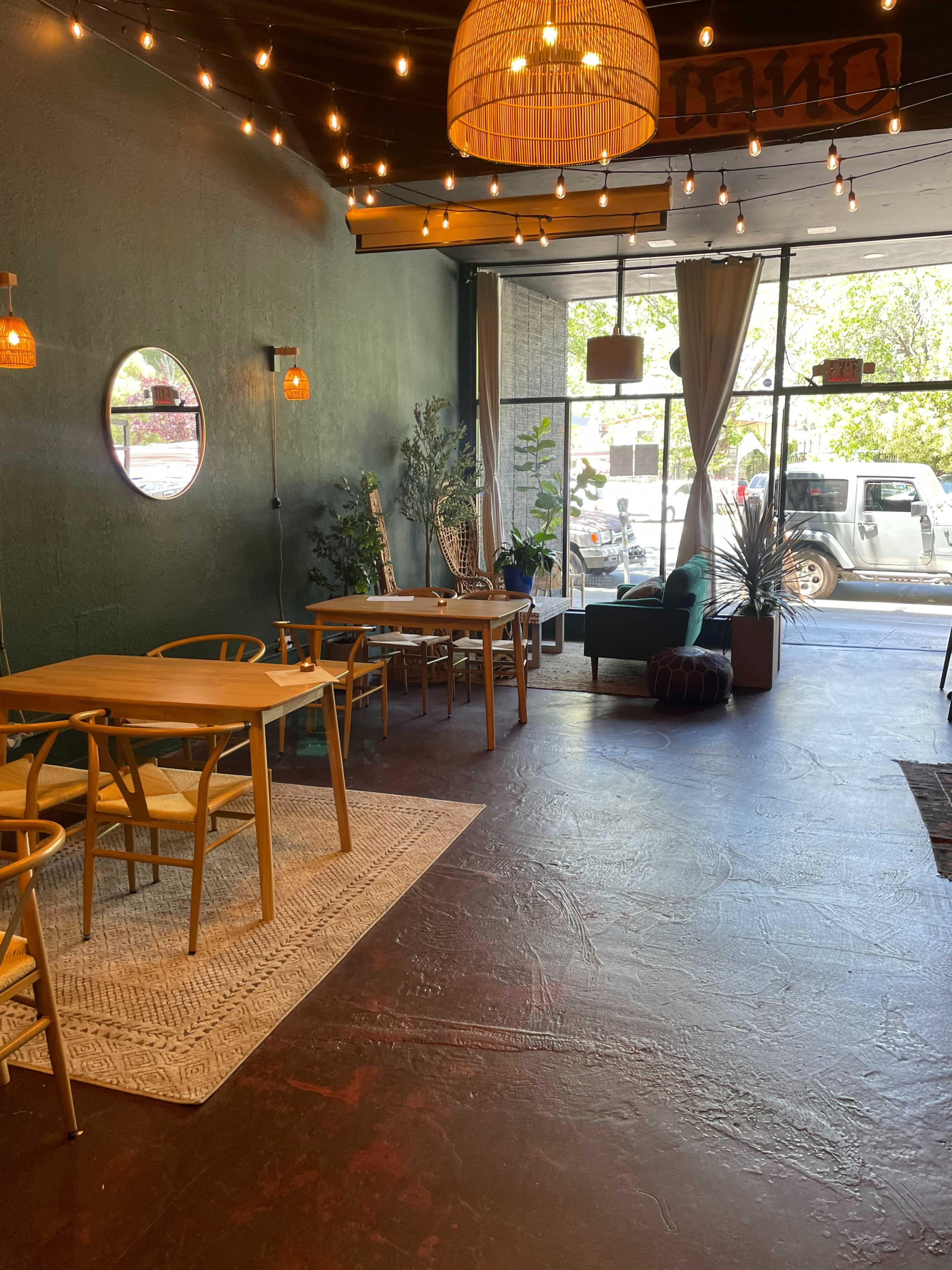 A cafe interior with wooden tables, a large window displaying outdoor scenery, and string lights hanging from the ceiling.