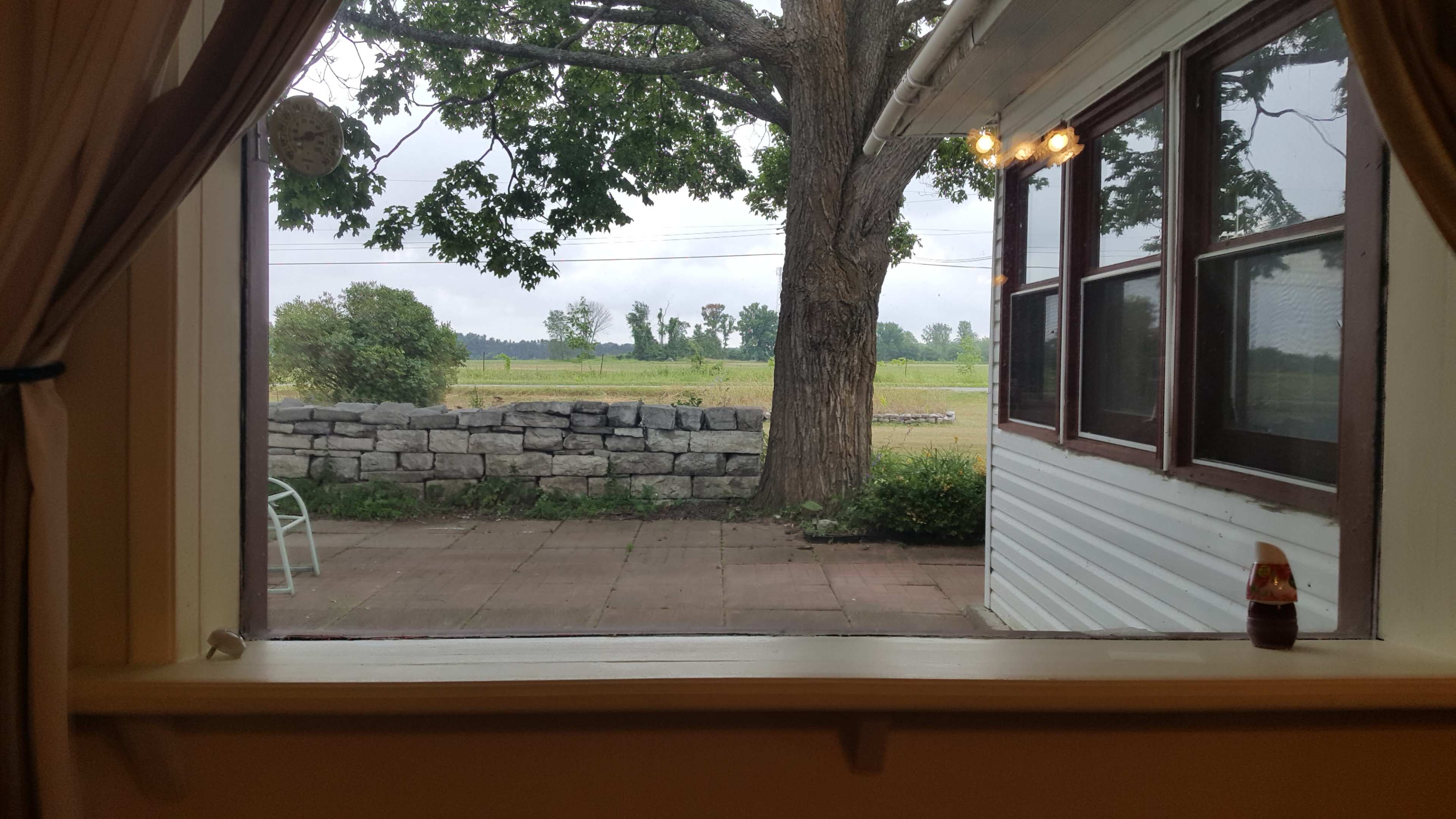 The view from the window shows a stone wall with a grassy field and trees in the background under an overcast sky.
