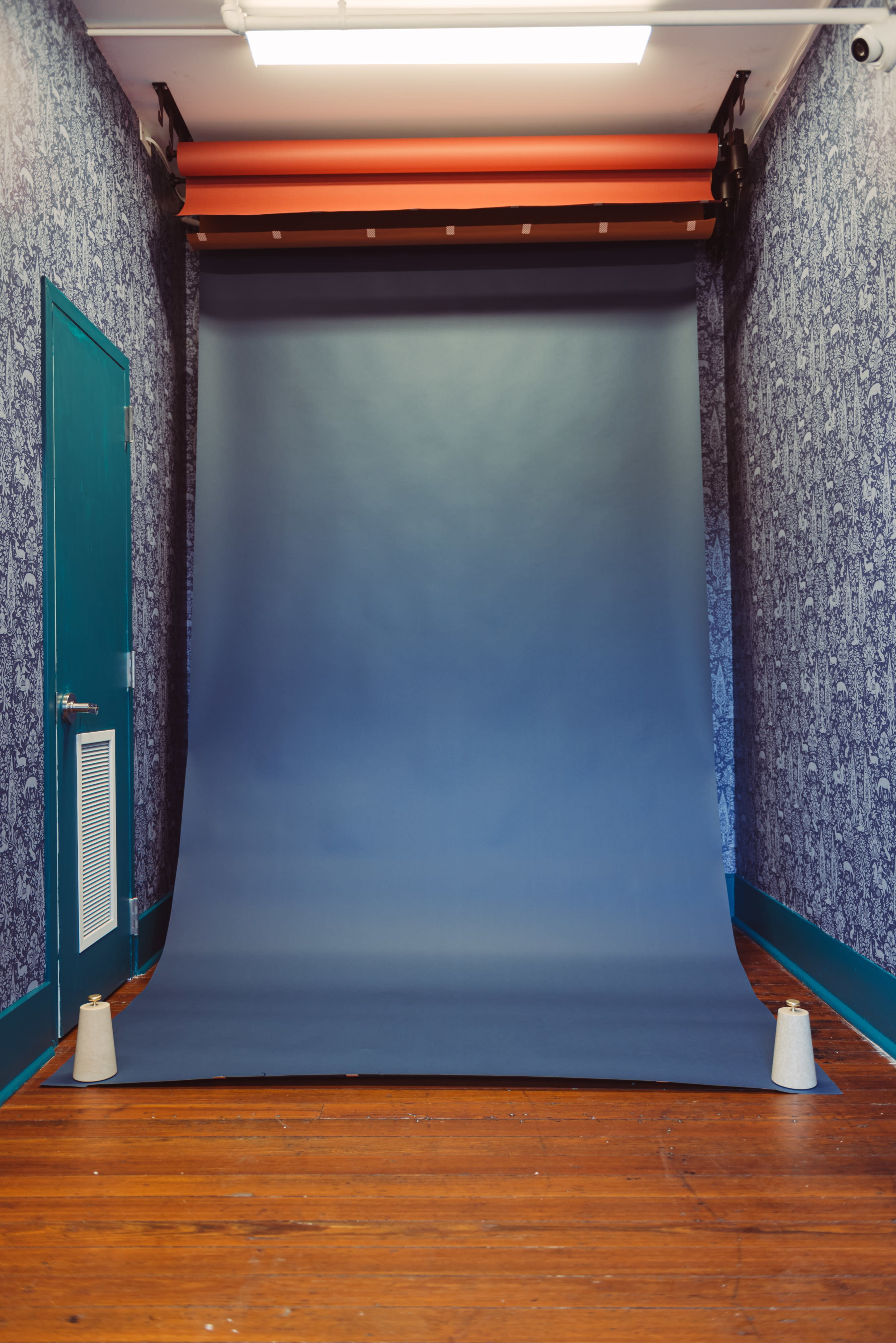 A smooth gray backdrop is set up against a patterned wall in a room with wooden floors.