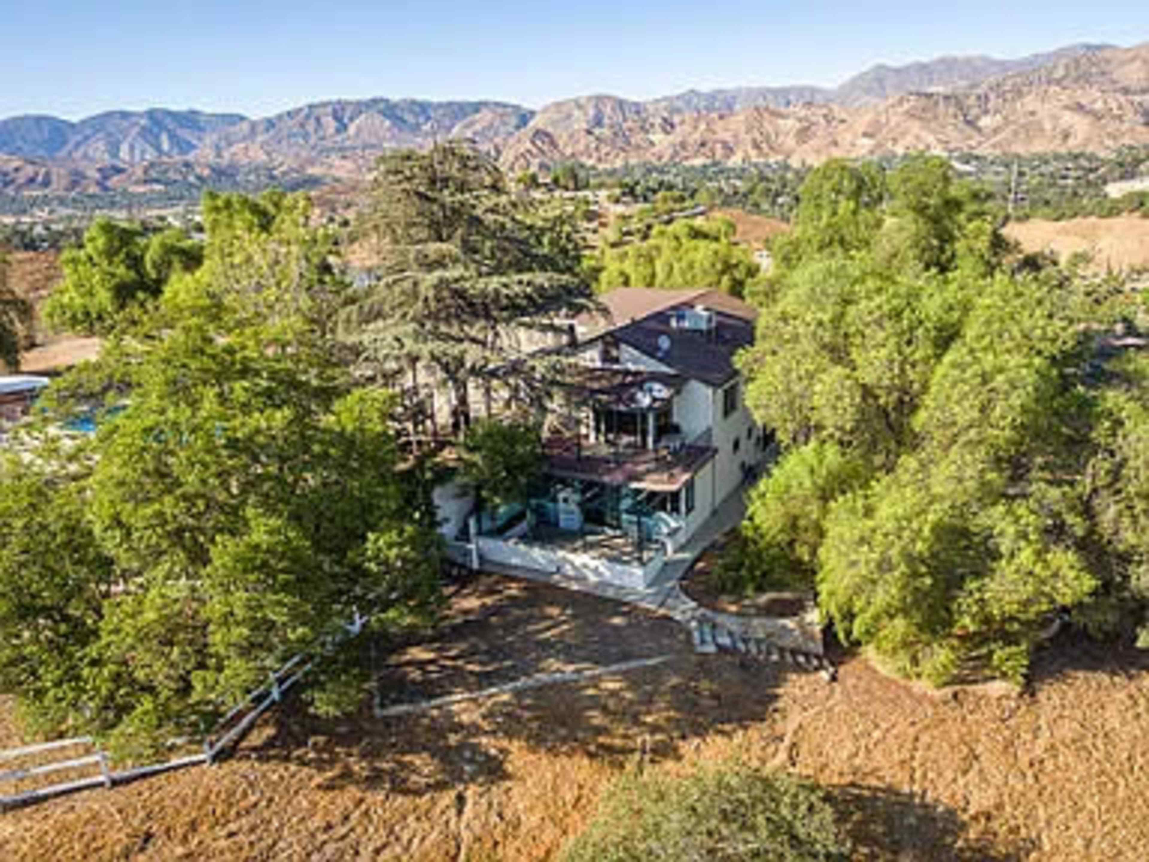 A two-story house is surrounded by trees and hills, with a deck overlooking the landscape.