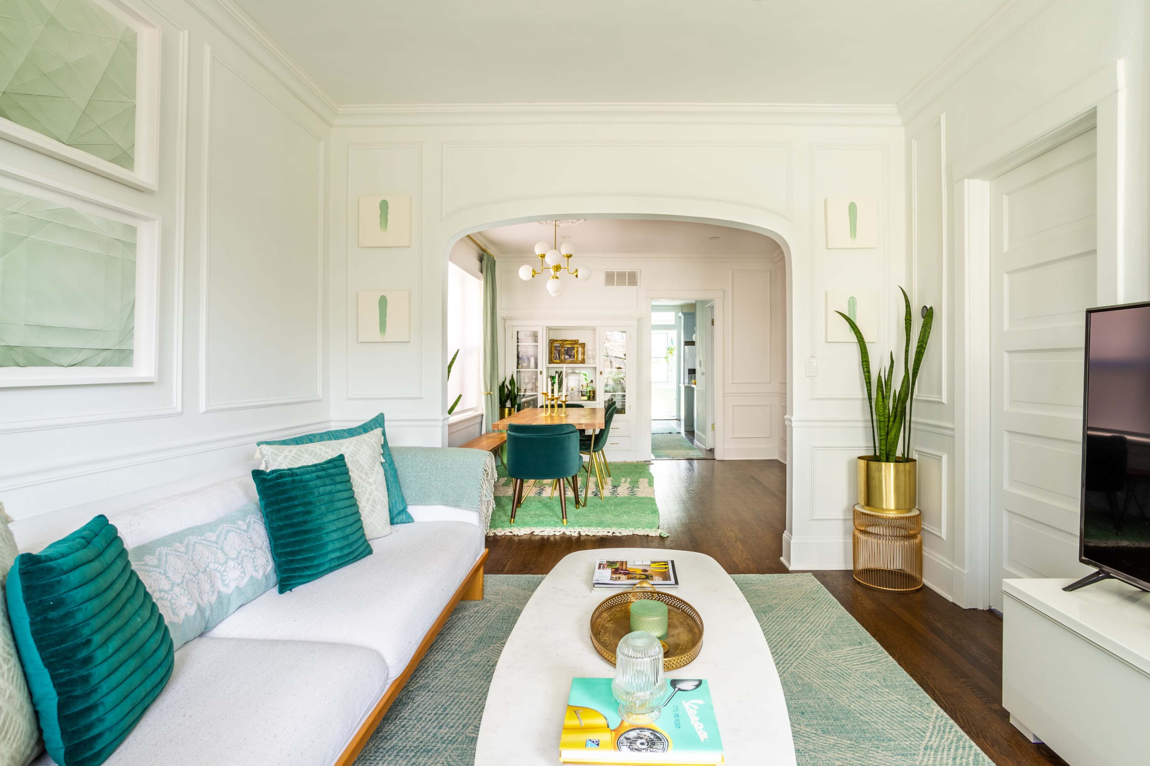 A modern living room with a gray and teal sofa, a marble coffee table, and a view into a dining area with green chairs and a white ceiling.