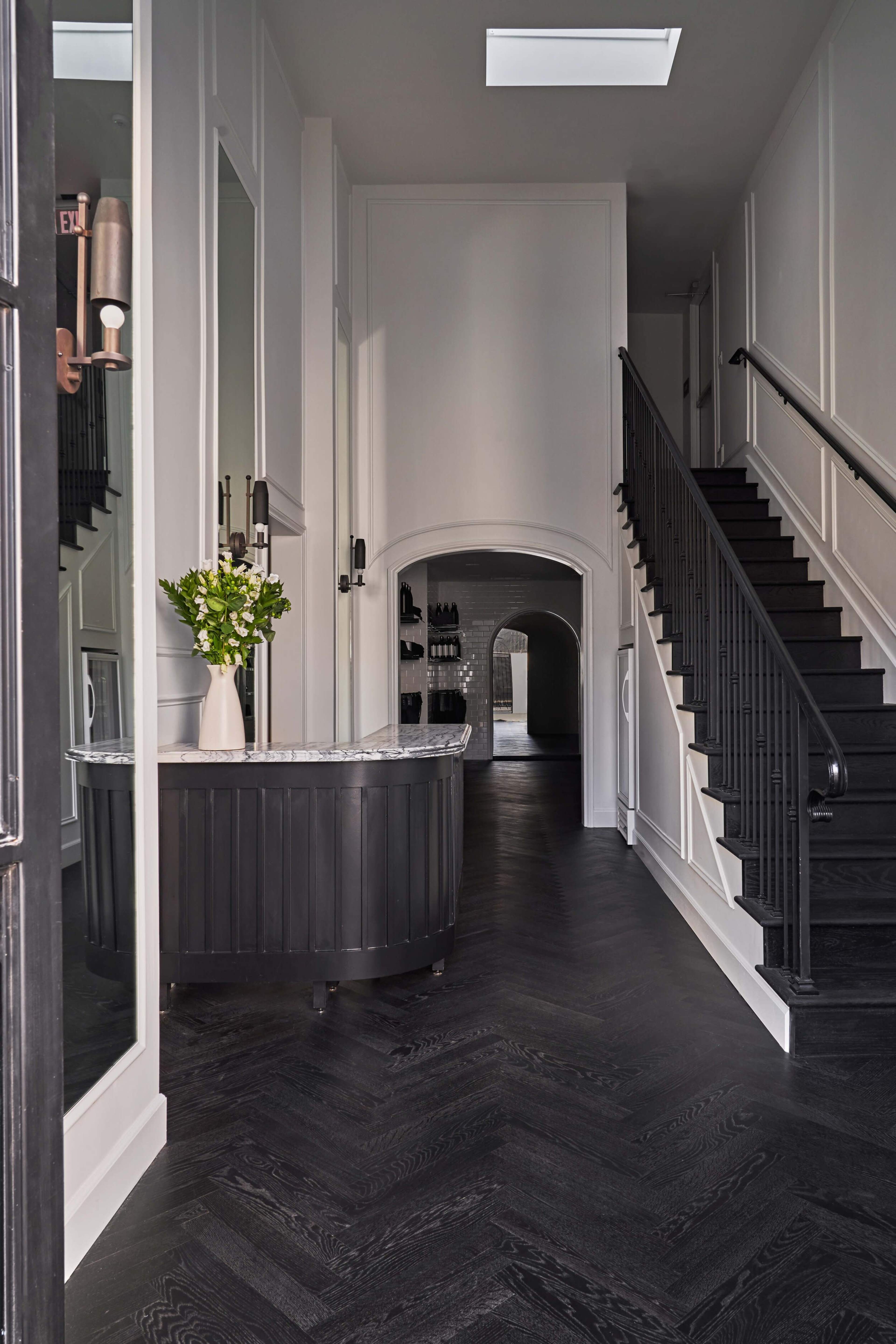 A narrow hallway features a marble-topped reception desk with a vase of flowers, leading to a staircase and an arched entryway.