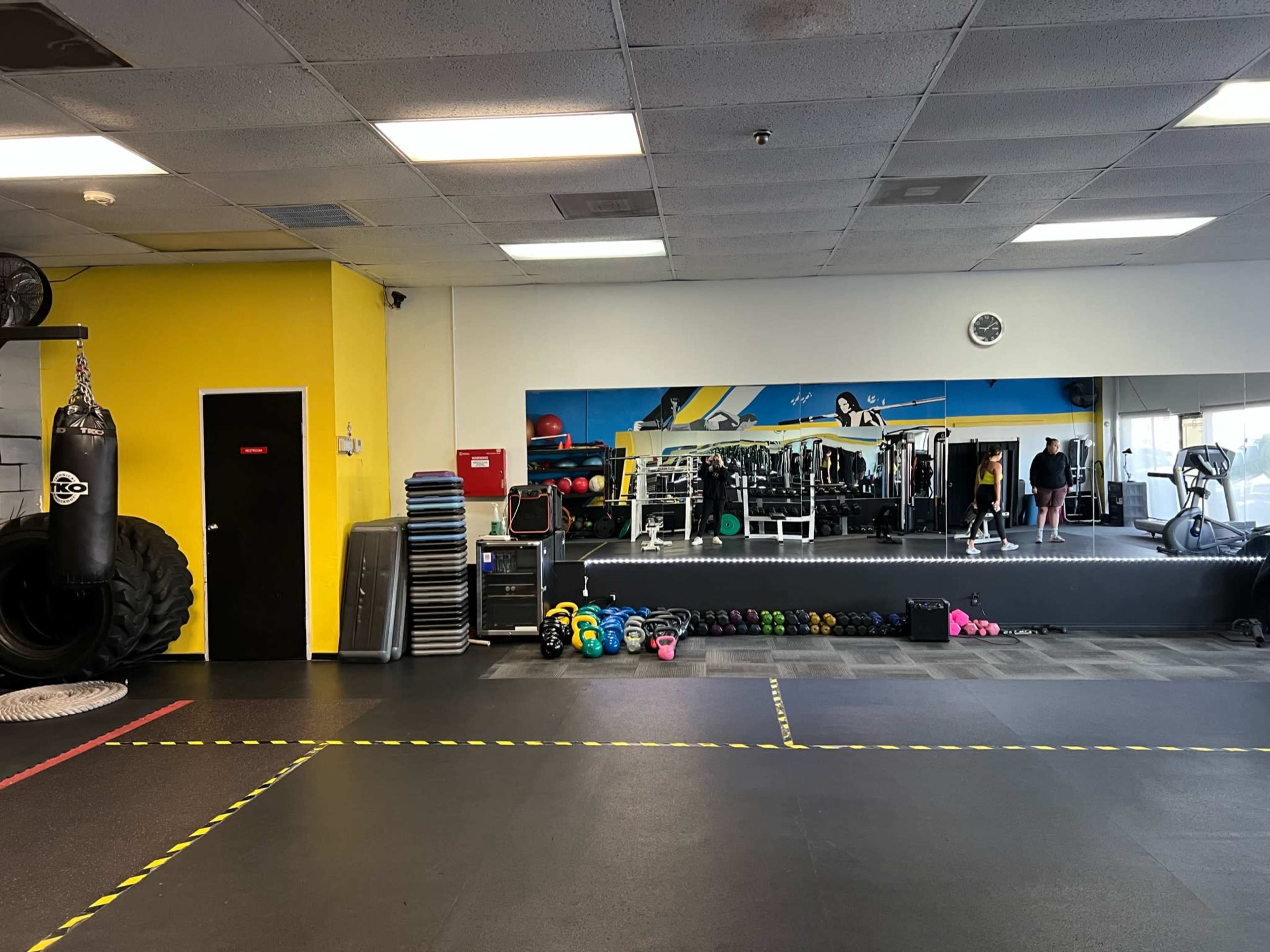 A well-organized gym interior featuring exercise equipment, a boxing bag, and colorful weights on the floor.