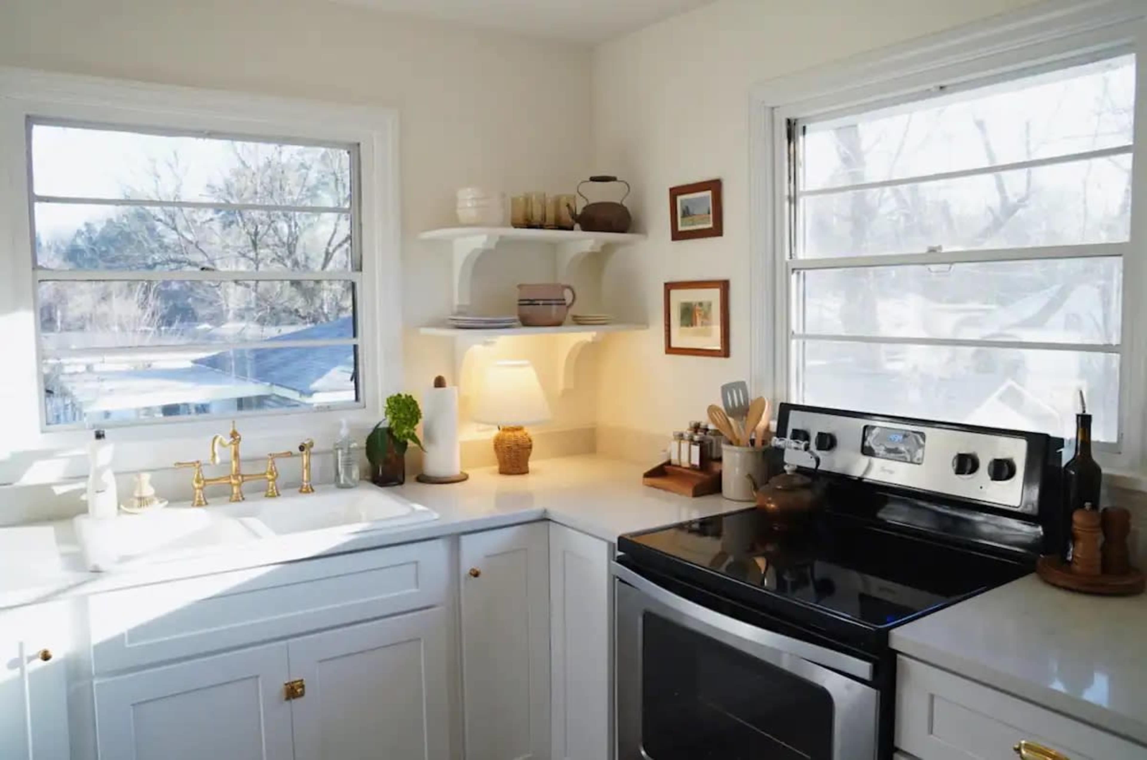 A well-lit kitchen featuring a stainless steel stove, white cabinetry, and open shelving displaying various kitchen items.