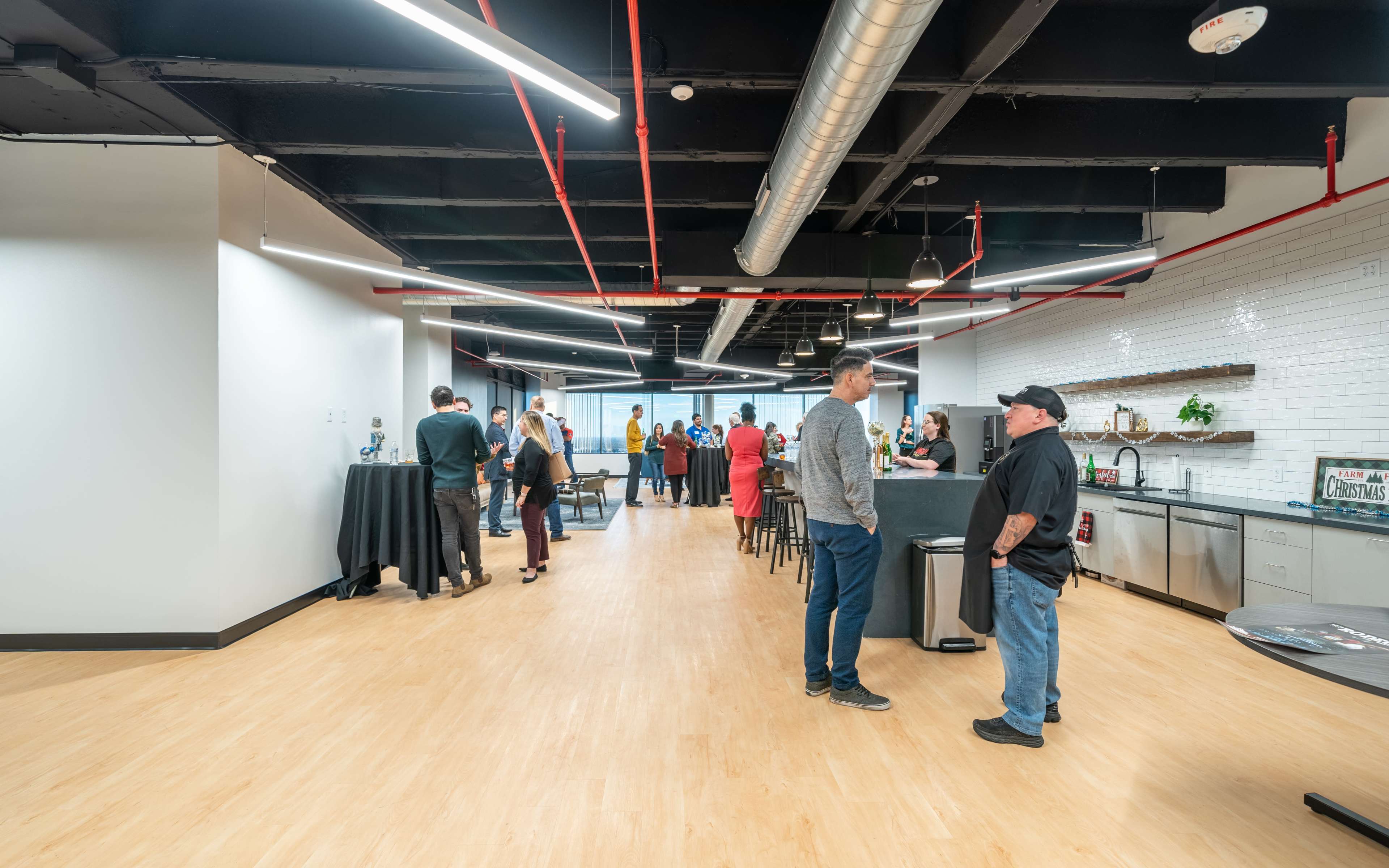 A group of people is gathered in a modern office space with a kitchen area, engaging in conversations and networking.
