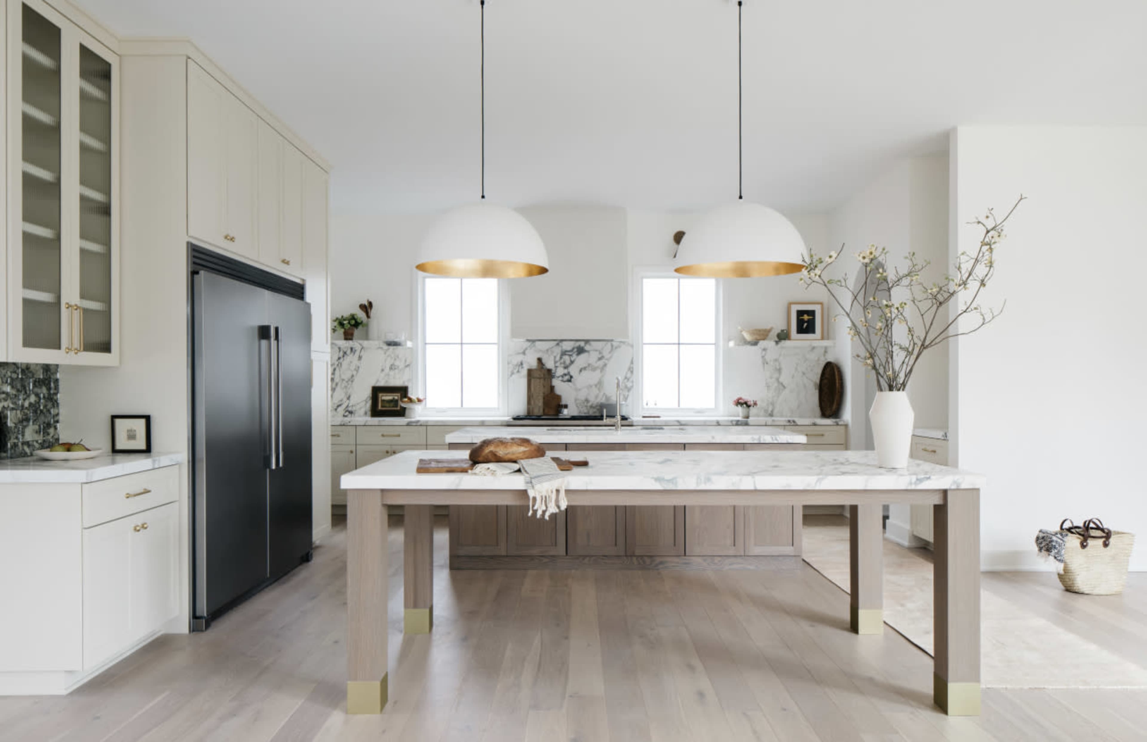 A modern kitchen features a marble-topped island with two large pendant lights, sleek cabinetry, and a dark refrigerator.