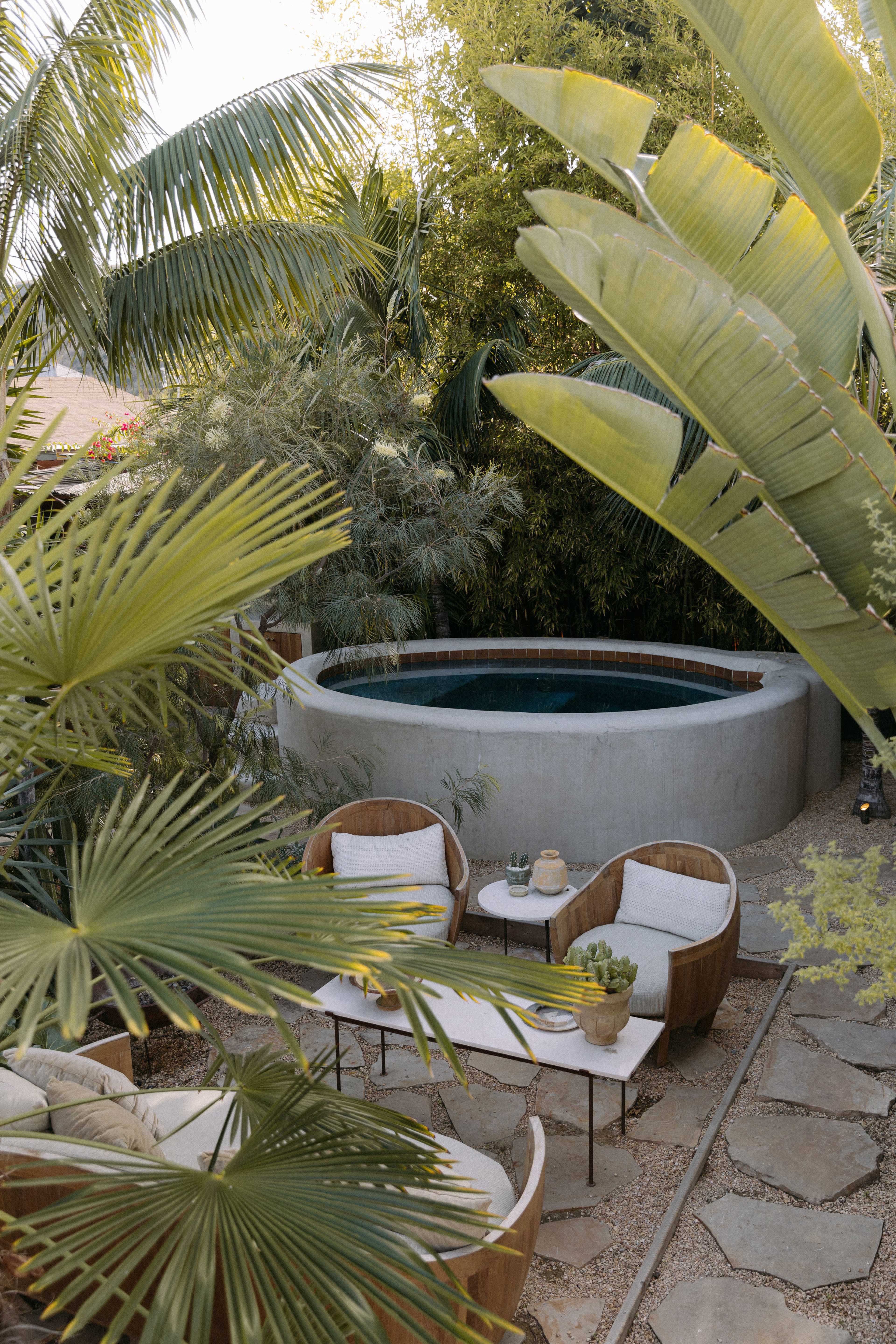 A secluded backyard features a circular plunge pool surrounded by lush greenery and outdoor seating.