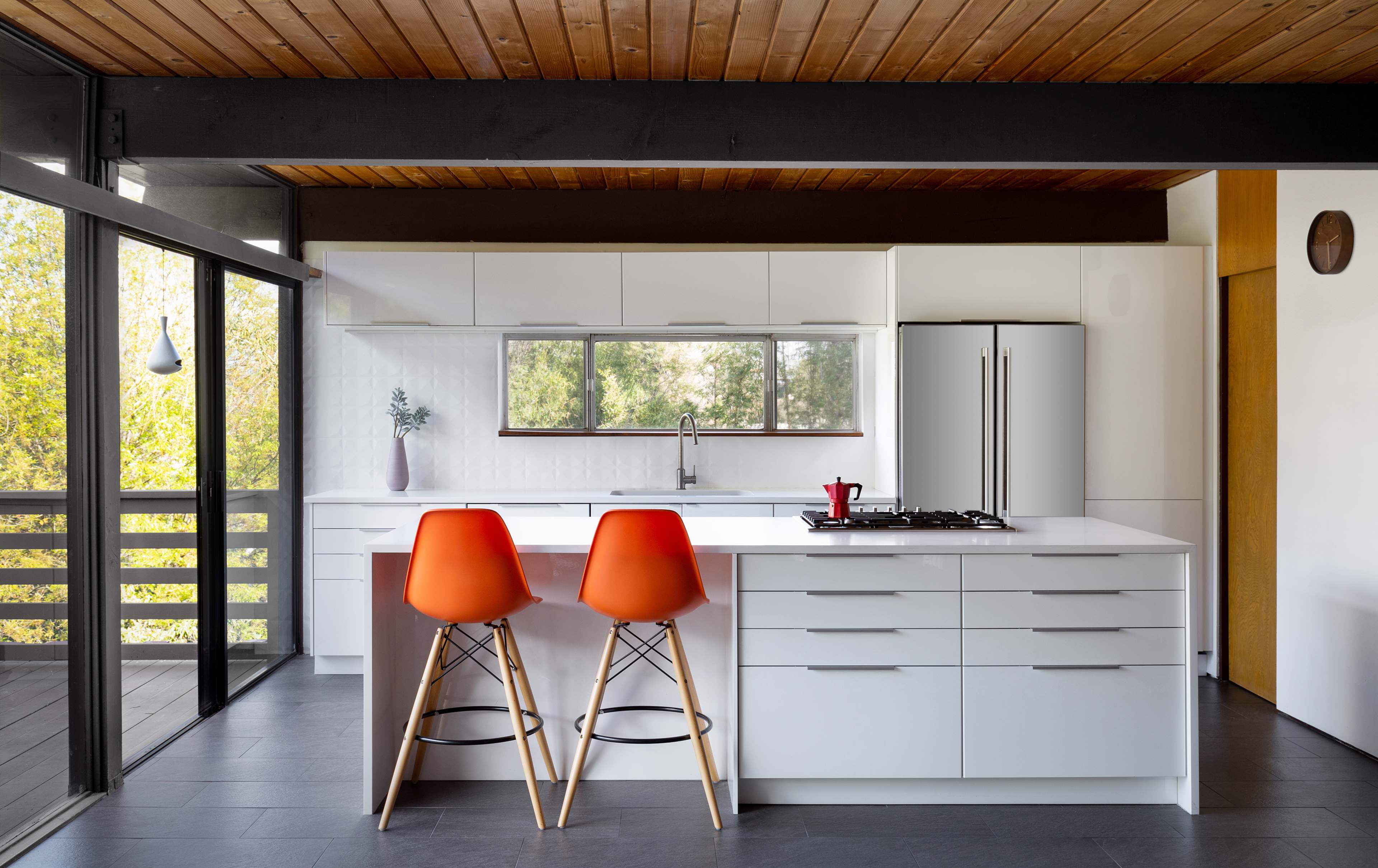 A modern kitchen features a white cabinetry, a large island with two orange bar stools, and stainless steel appliances.