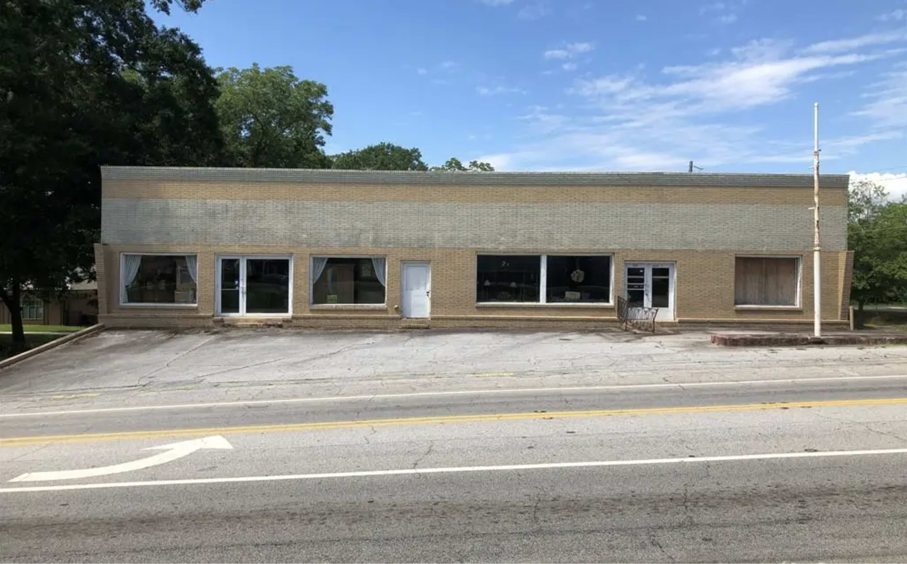 The image shows a single-story brick building with large front windows, situated on a sloped road.