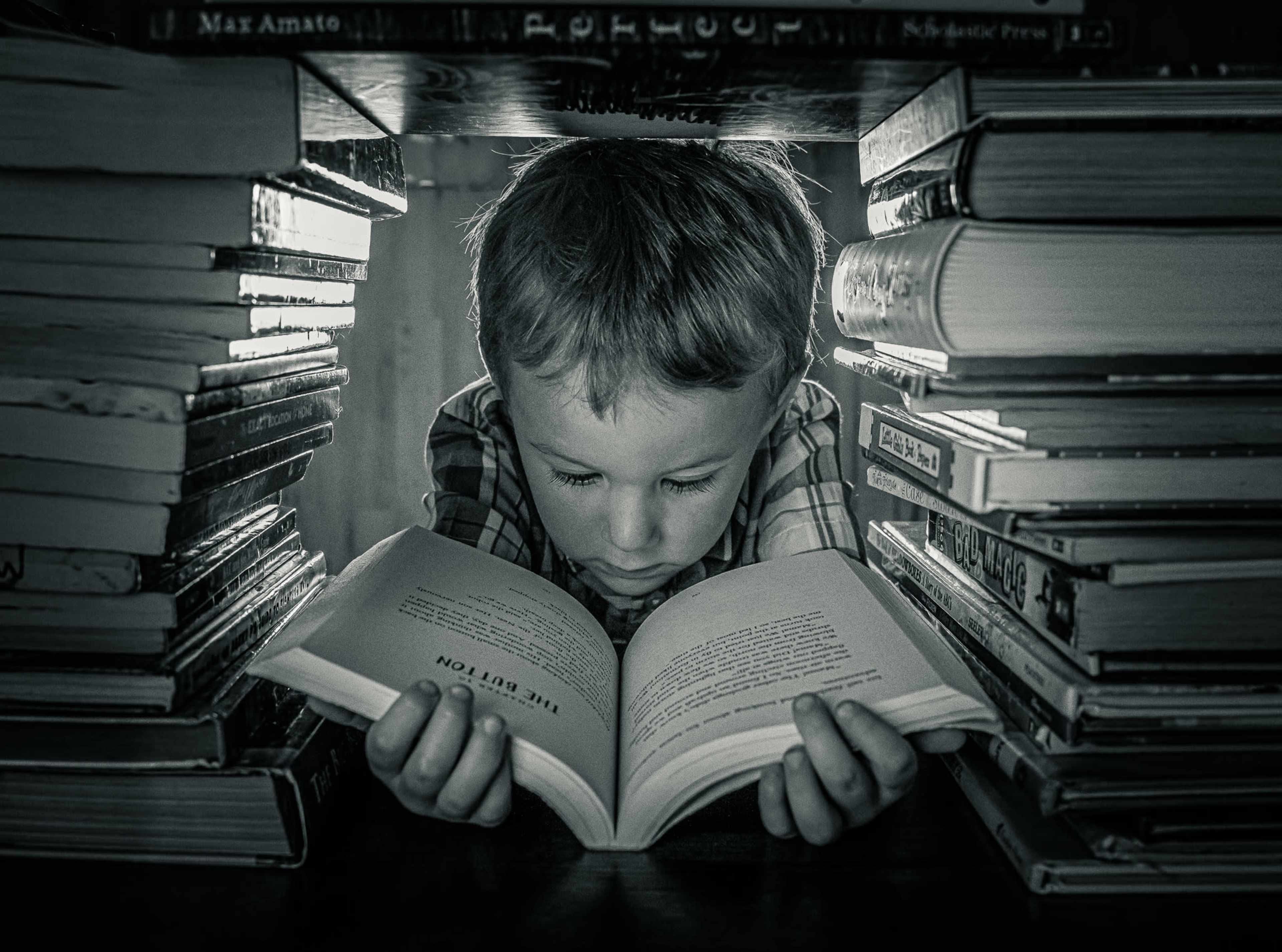 A child is reading a book while seated between stacks of books.