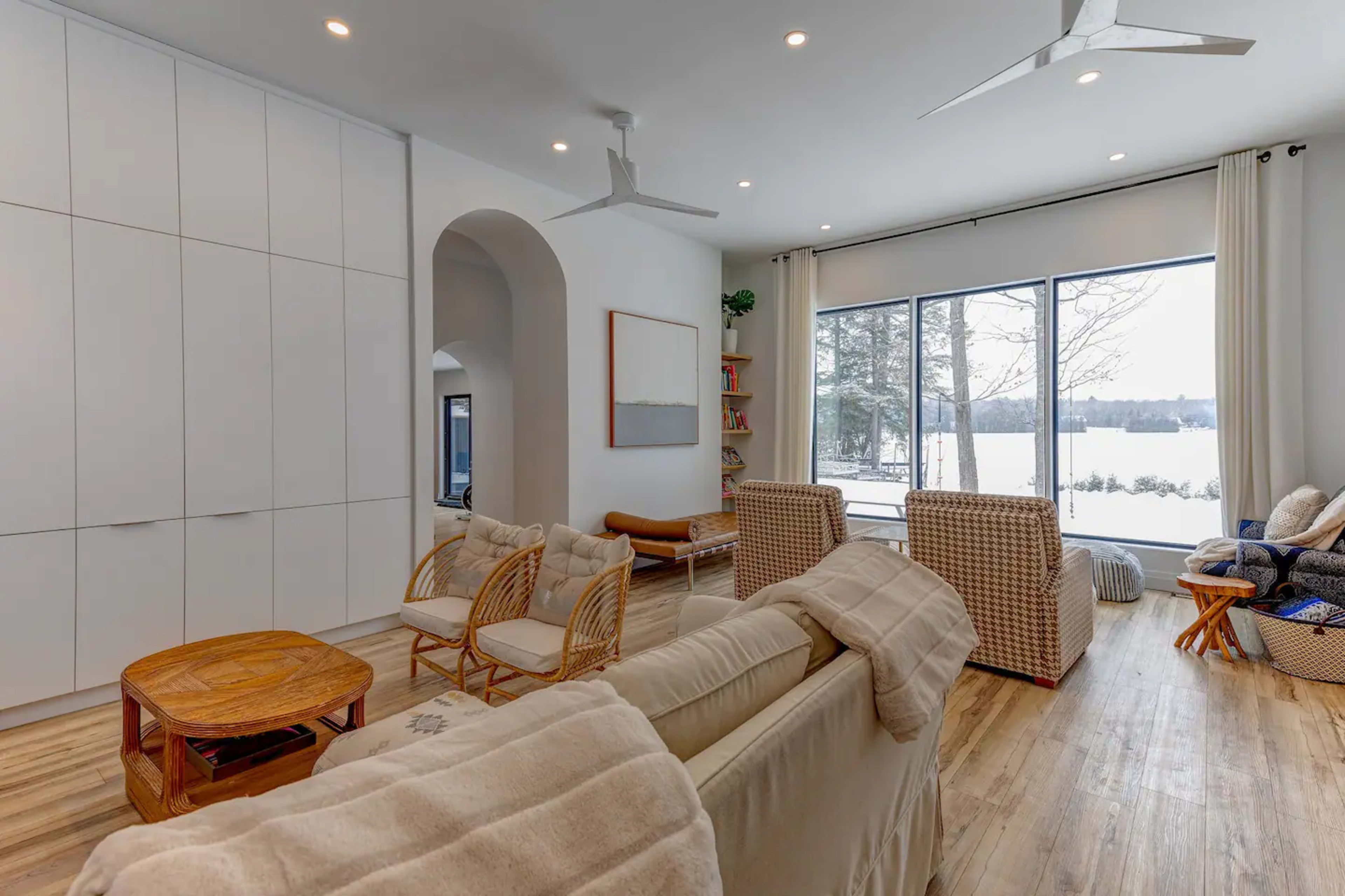 A modern interior space features light-colored furniture, large windows with a view of nature, and comfortable seating arranged around a coffee table.