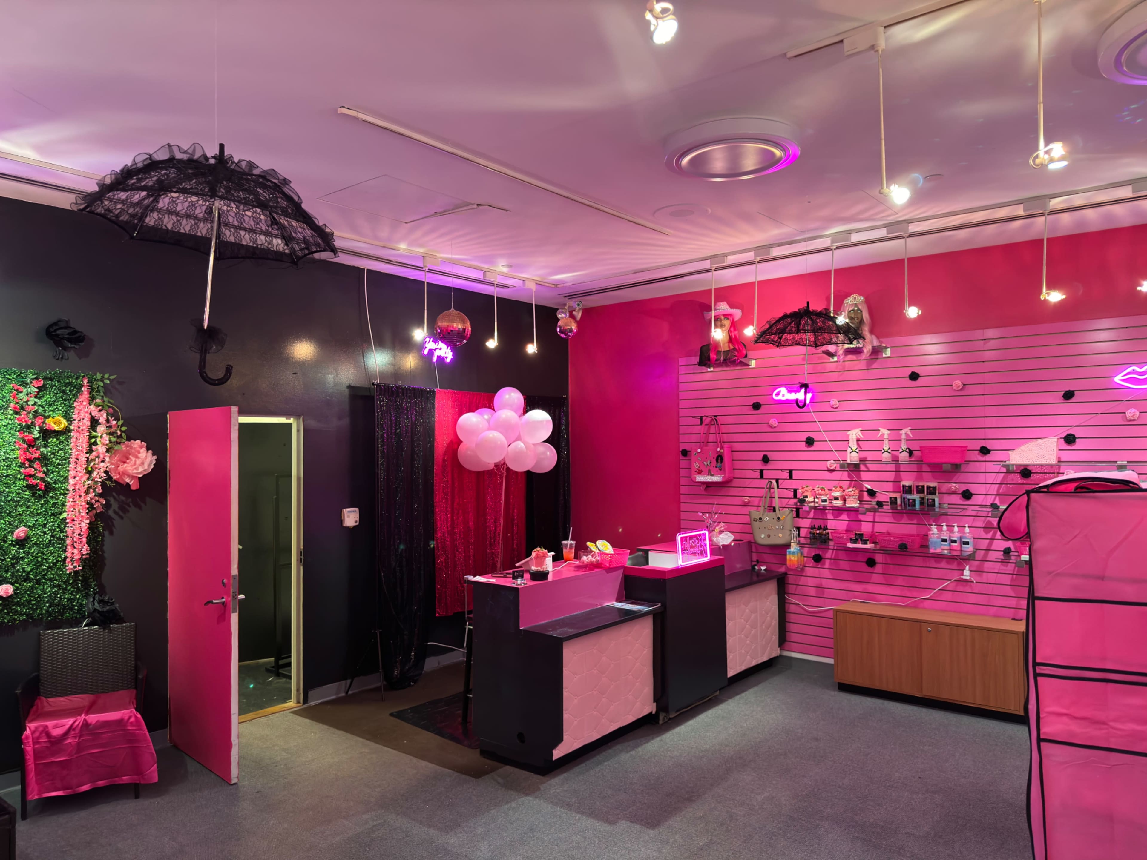 A brightly colored boutique features a reception desk adorned with pink decor, umbrellas hanging from the ceiling, and various beauty products displayed on the walls.