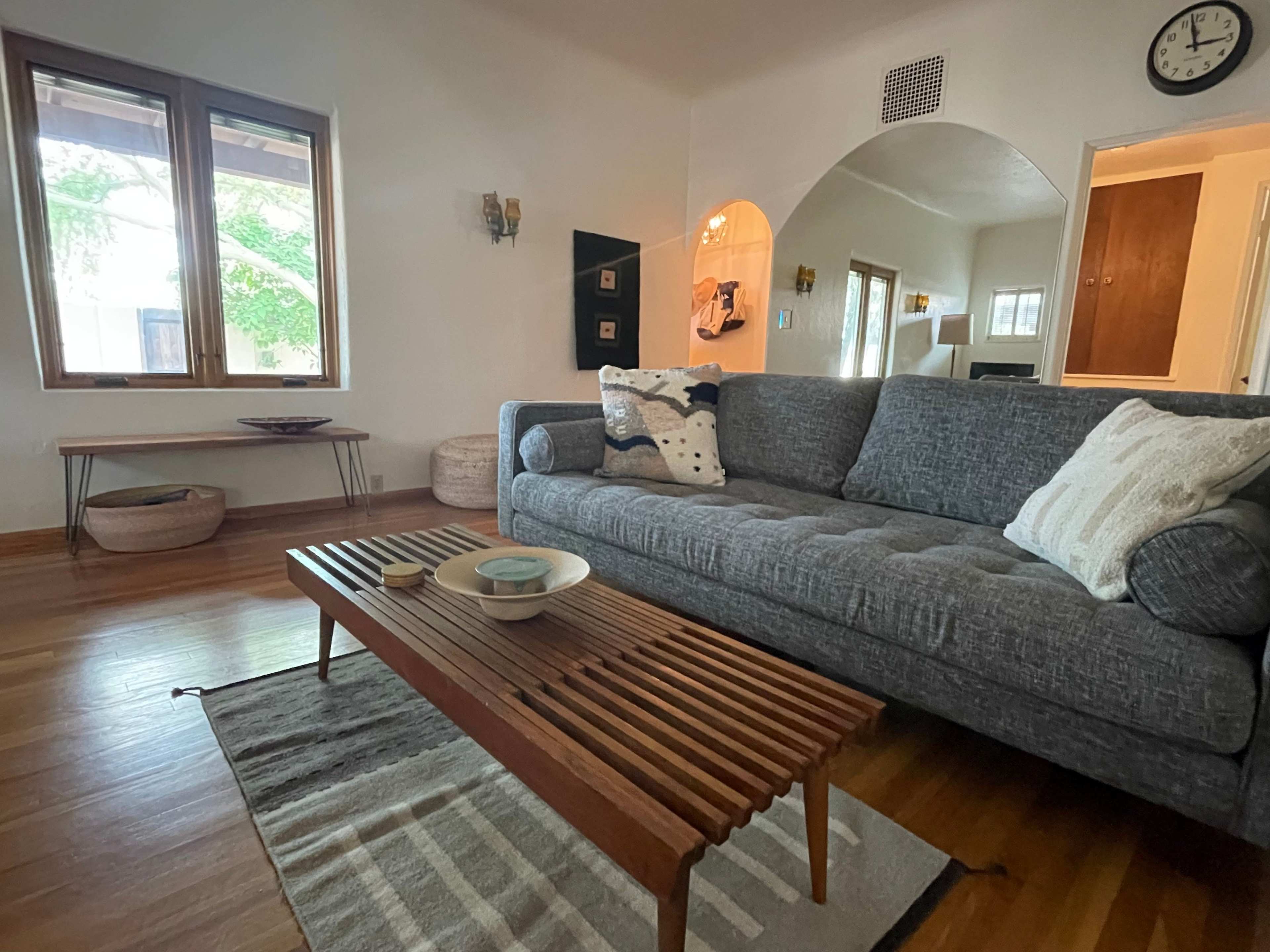 A living room featuring a gray couch, a wooden coffee table, and large windows allowing natural light in.