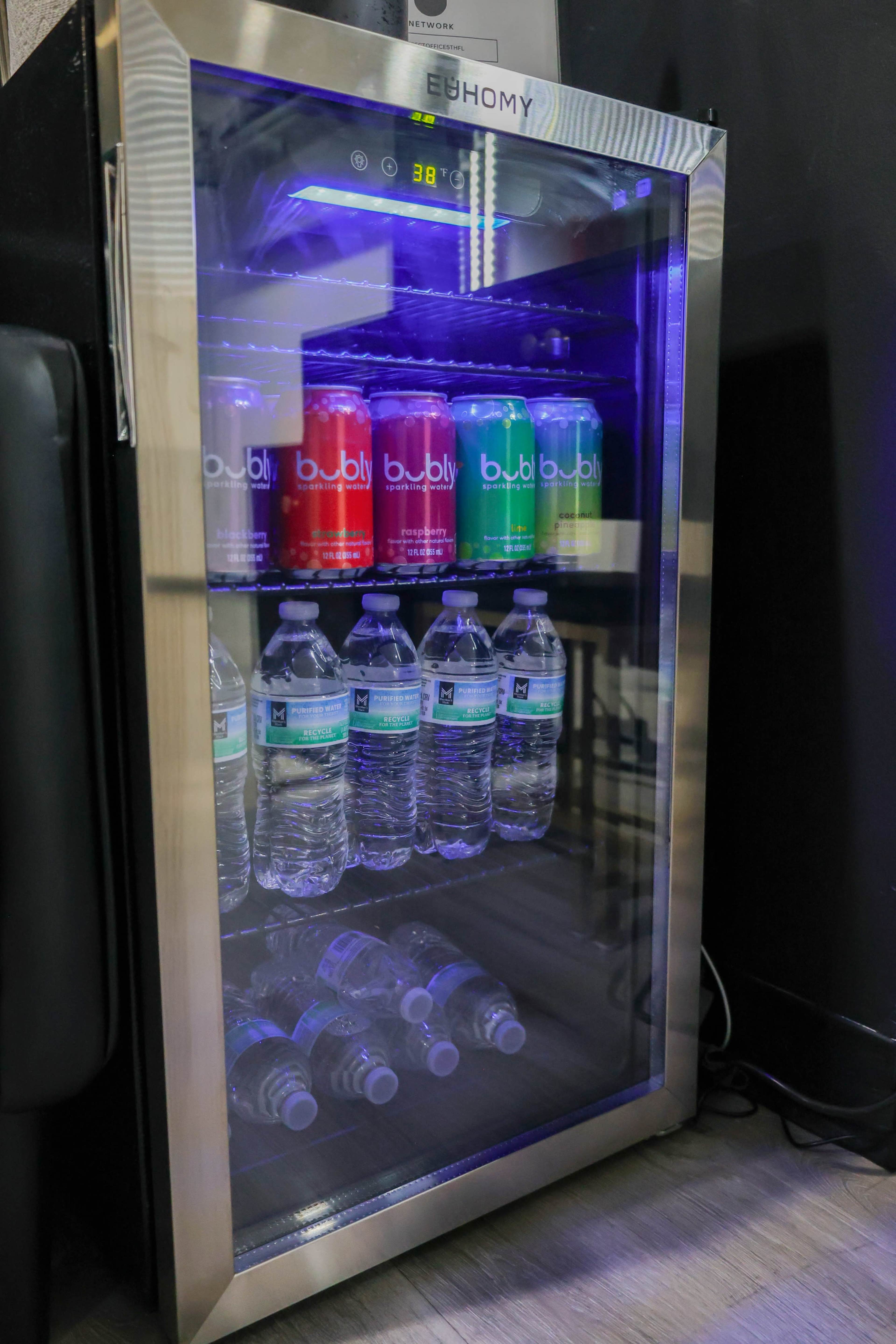 A glass-front beverage cooler displays various cans of Bubly sparkling water and bottles of water on its shelves.