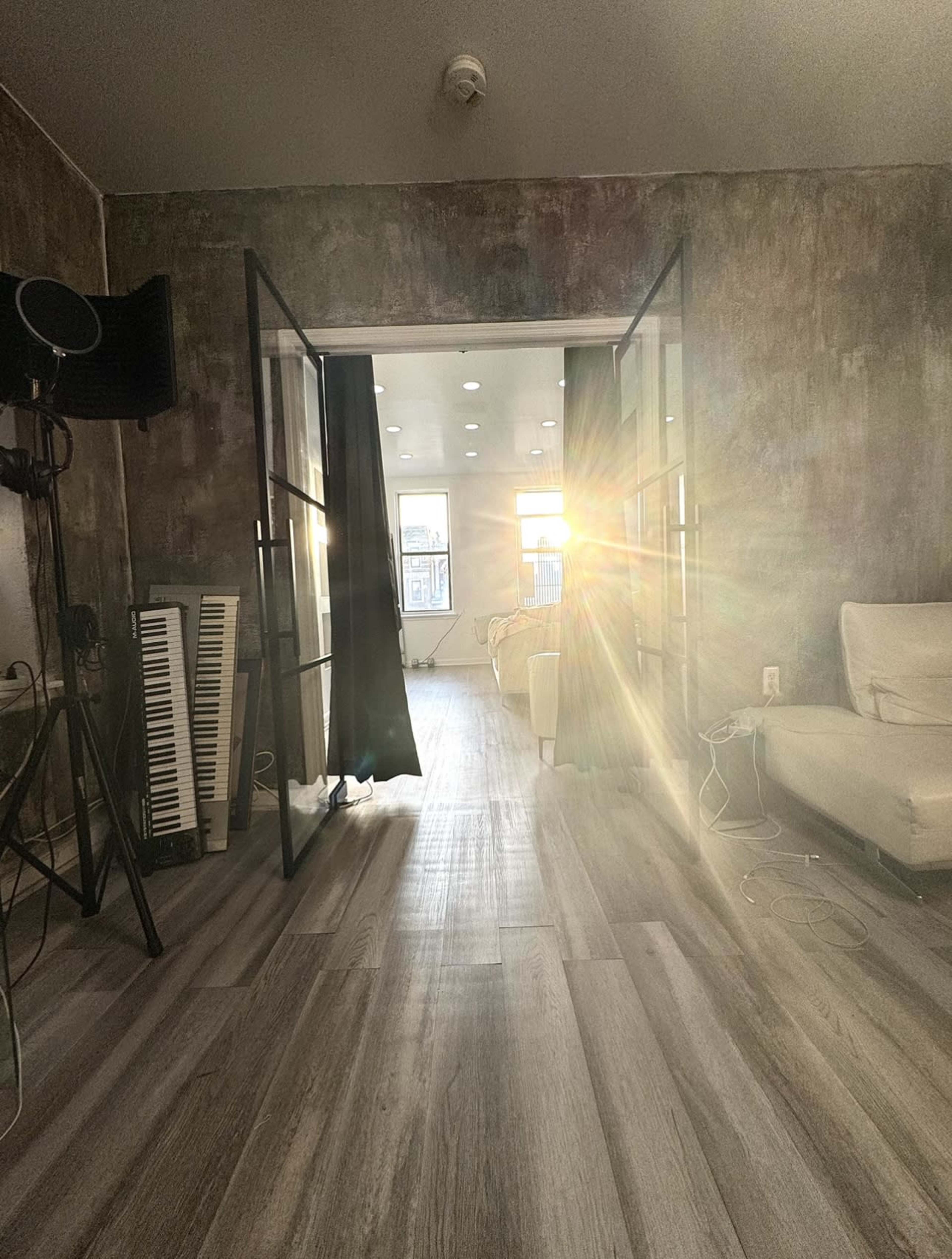 A sunbeam enters through an open doorway, illuminating a modern interior space with a sofa and large windows.