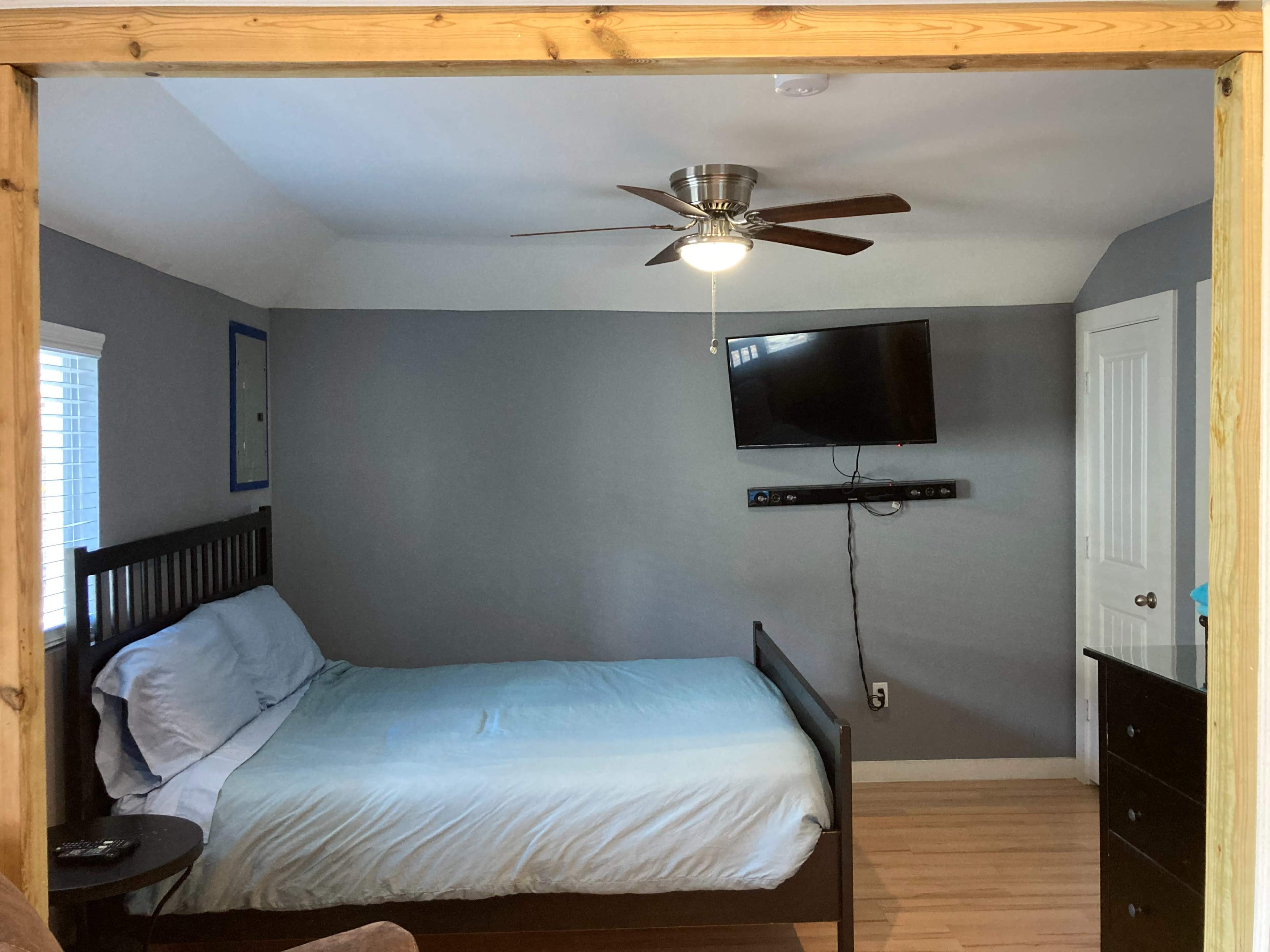 A bedroom with a bed, a television mounted on the wall, and a fan on the ceiling.