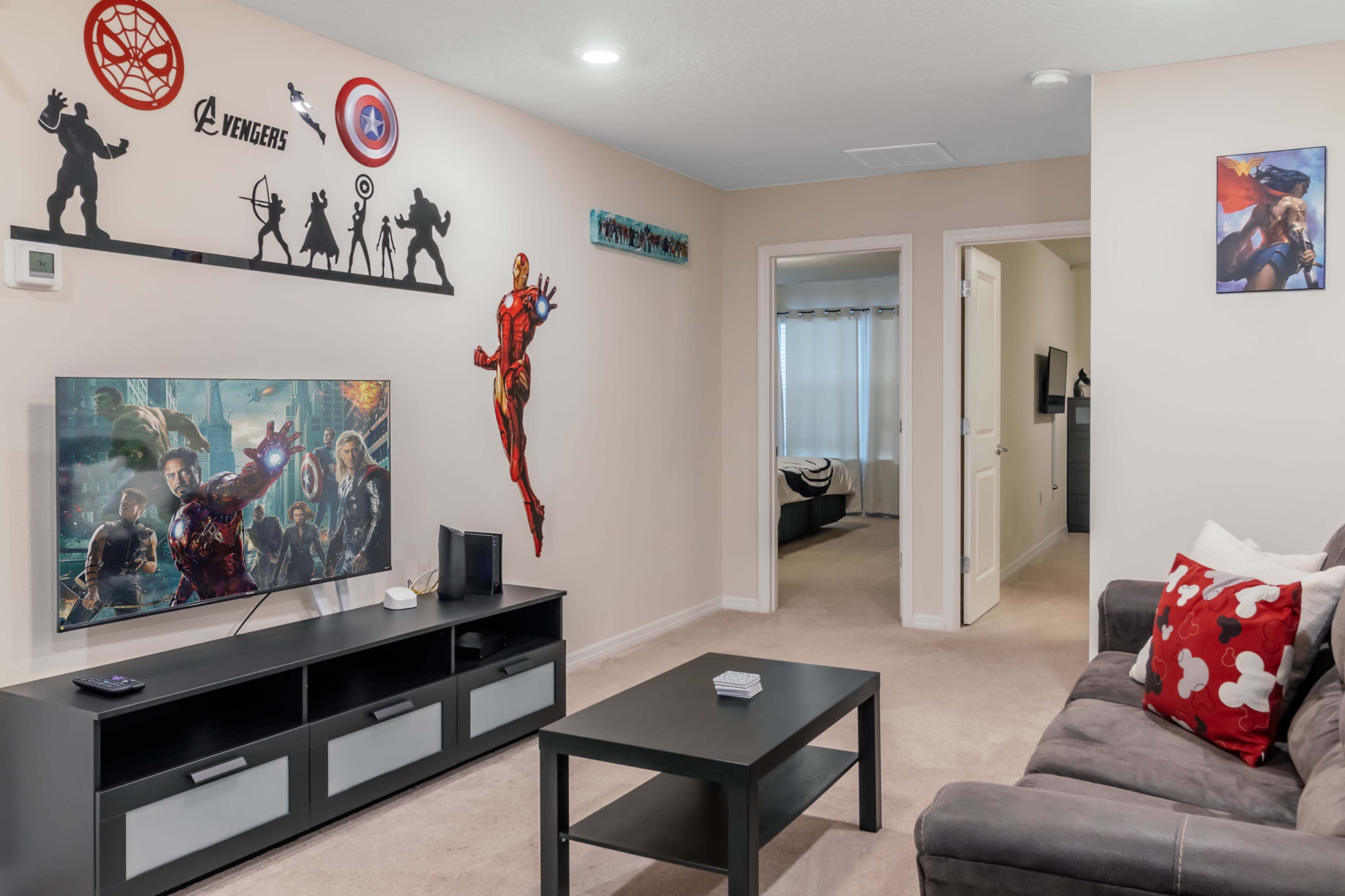 A living room with a television displaying superhero artwork, a black coffee table, and walls decorated with various superhero-themed decals.