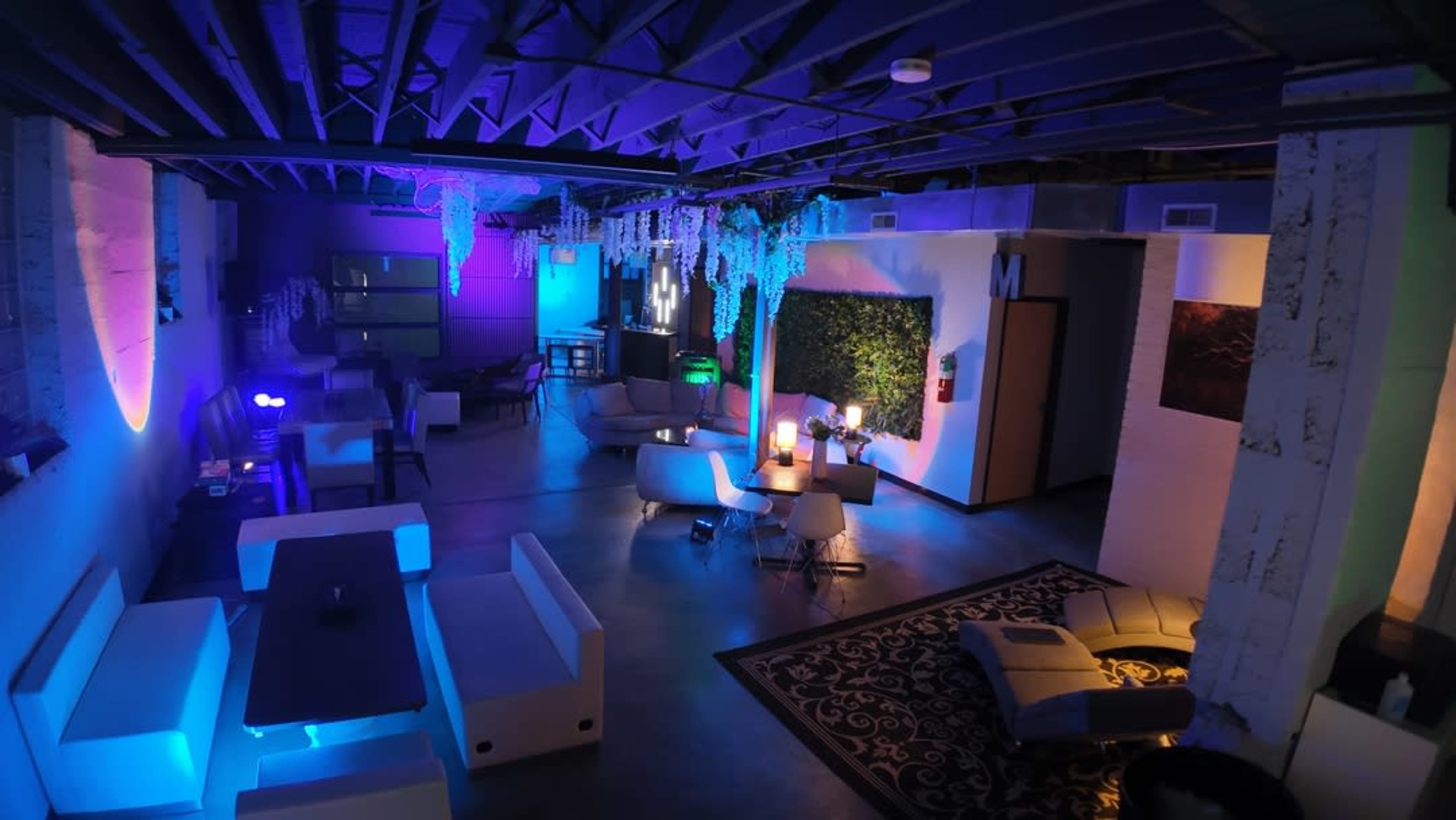 The image shows a dimly lit lounge with modern furniture, colorful lighting, and a blend of inviting seating areas.