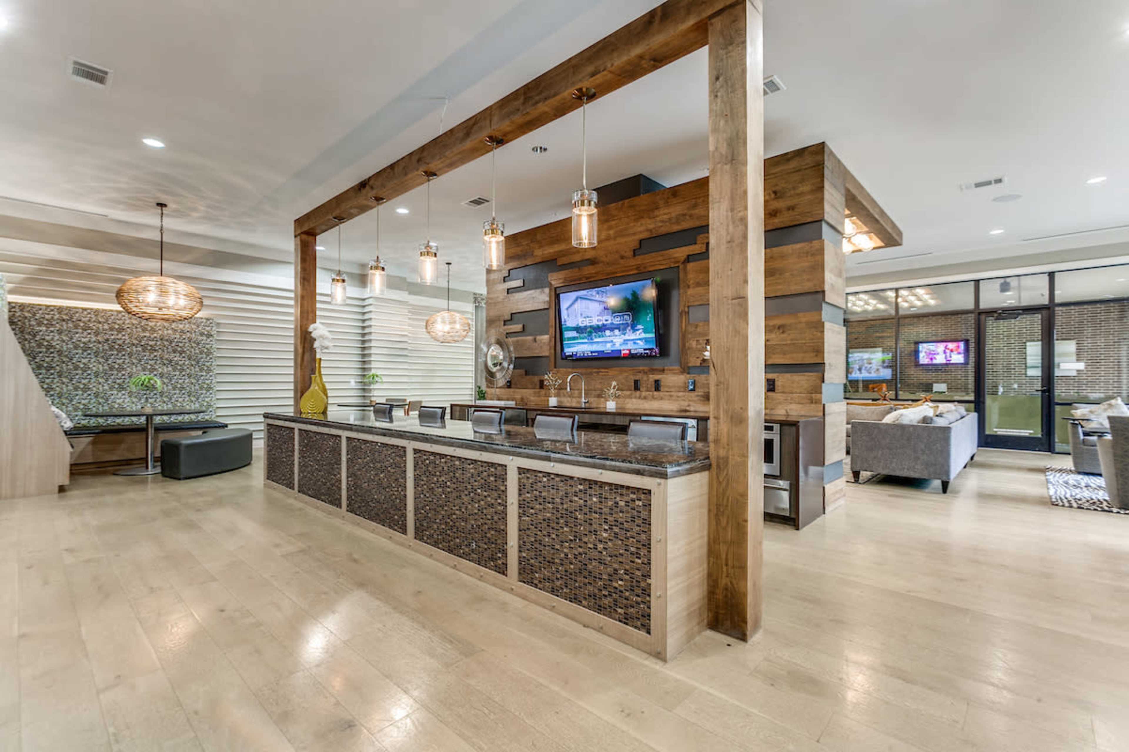 A modern lounge area with a large wooden bar, stone accents, and a television mounted on the wall, surrounded by seating arrangements.