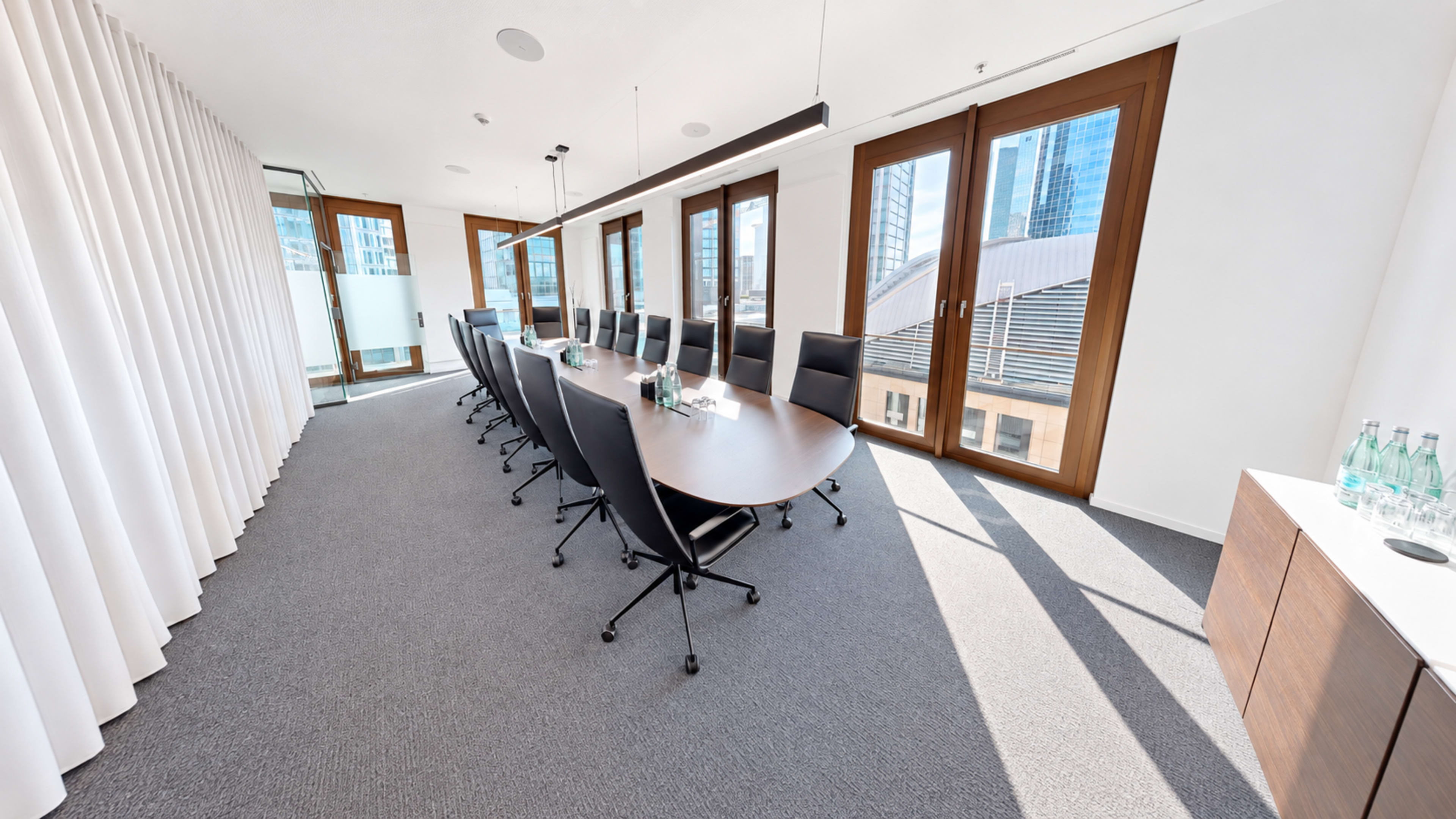 A modern conference room features a long table with black chairs and large windows letting in natural light.
