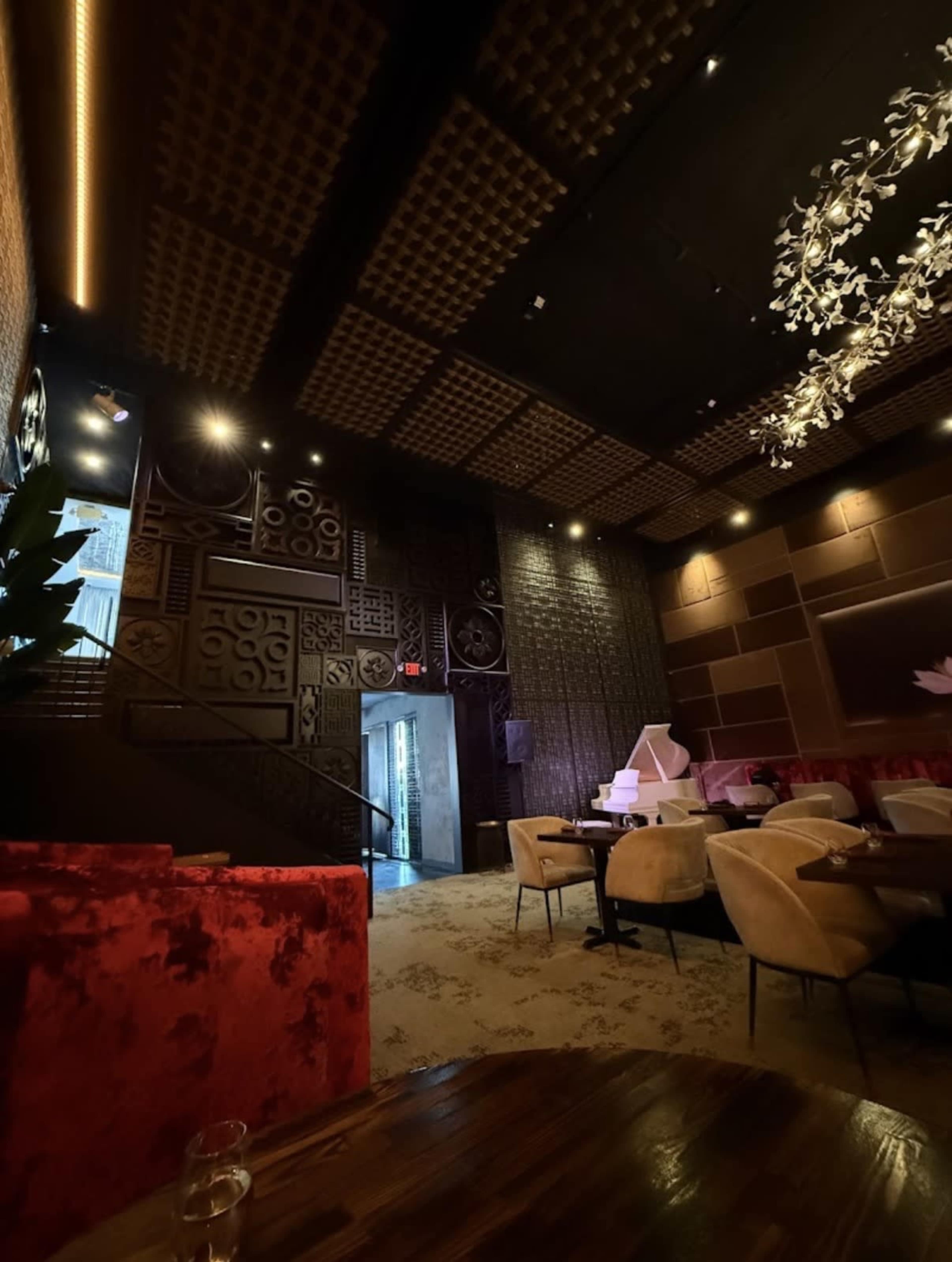 The image shows a dimly lit restaurant interior featuring plush seating, decorative wall panels, and an illuminated staircase.