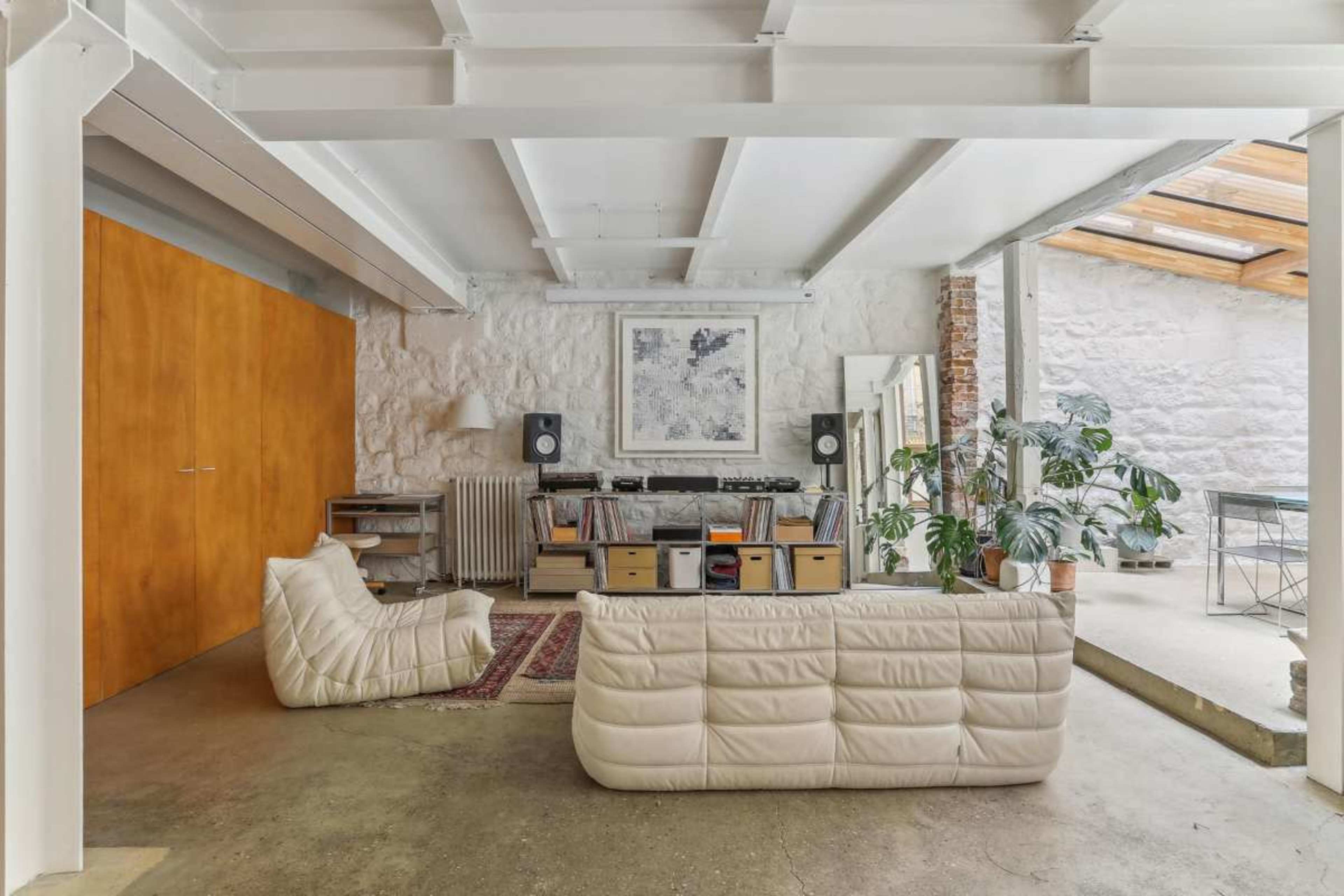 The image shows a modern living space with a white sofa, a record player setup, and a large window allowing natural light to enter.
