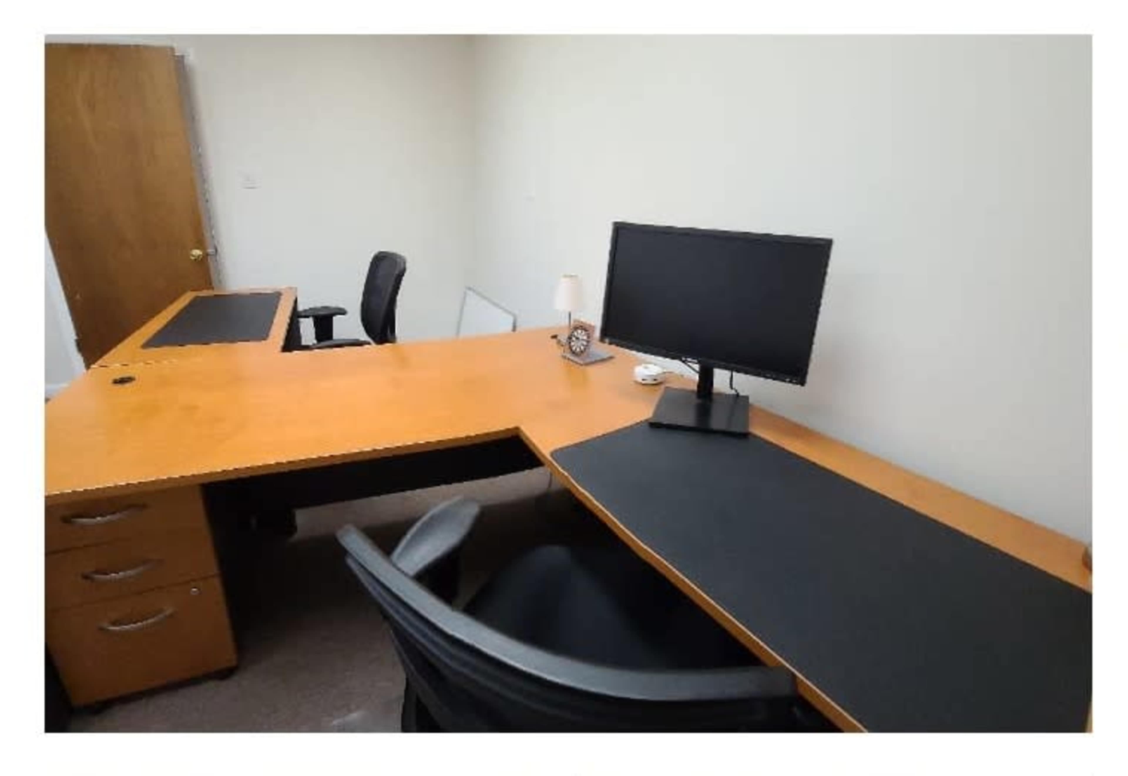 A dual-desk office setup with a computer monitor on one desk and a chair positioned in front of it.