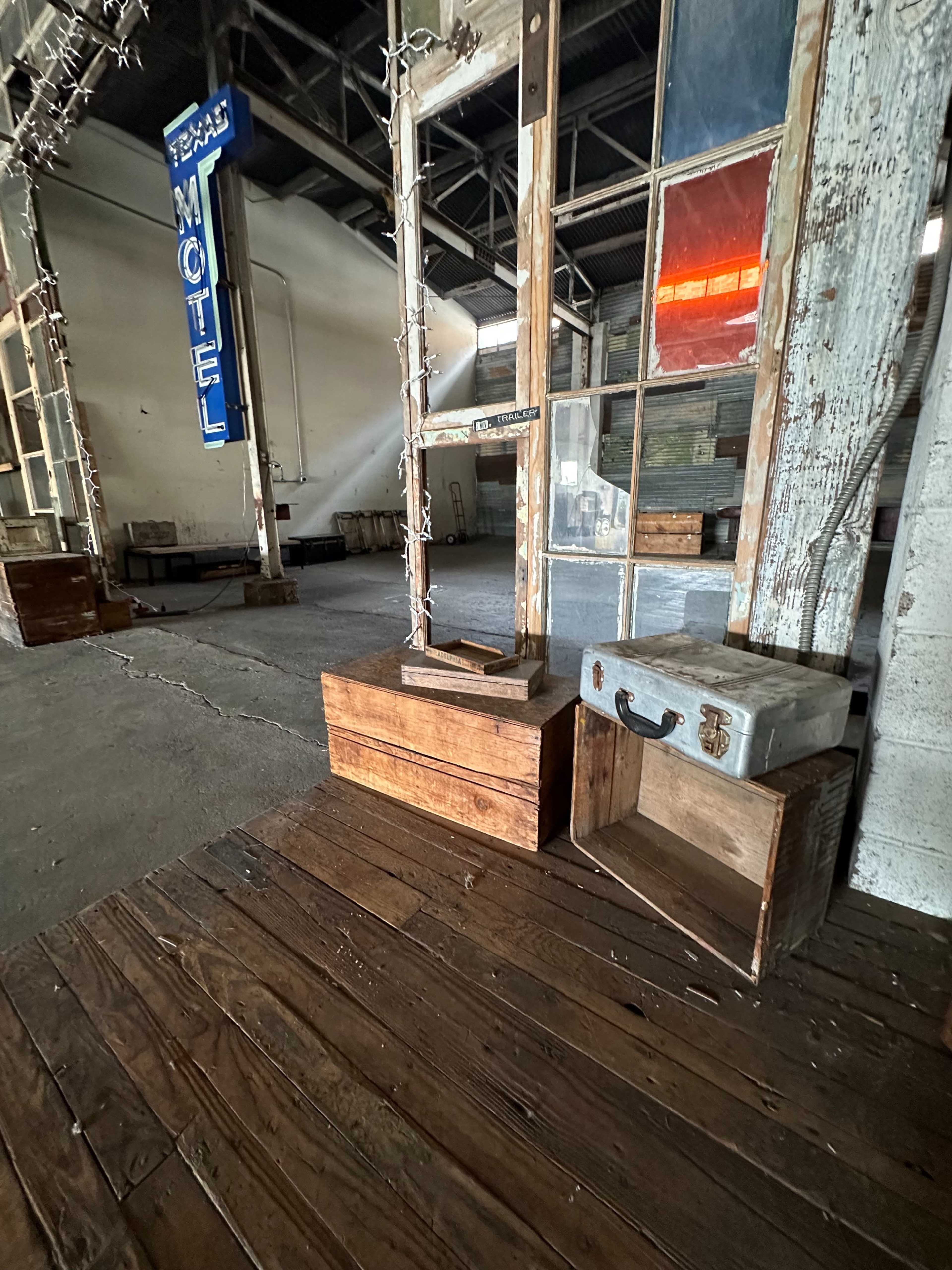An interior space with wooden flooring, various wooden boxes, and a blue sign that reads "TEXAS MOTEL" in the background.
