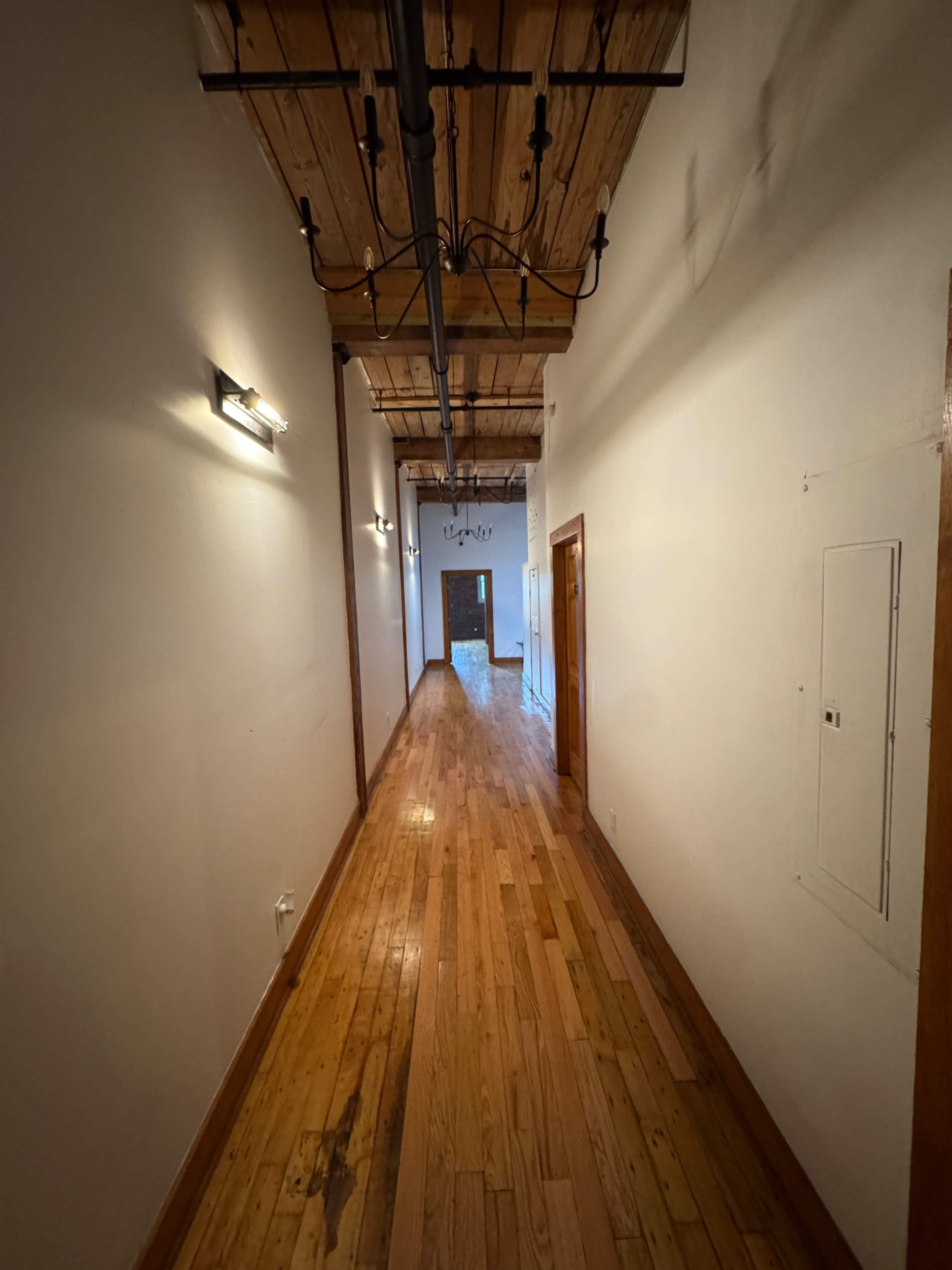 A long, narrow hallway features hardwood flooring and exposed wooden beams along the ceiling.