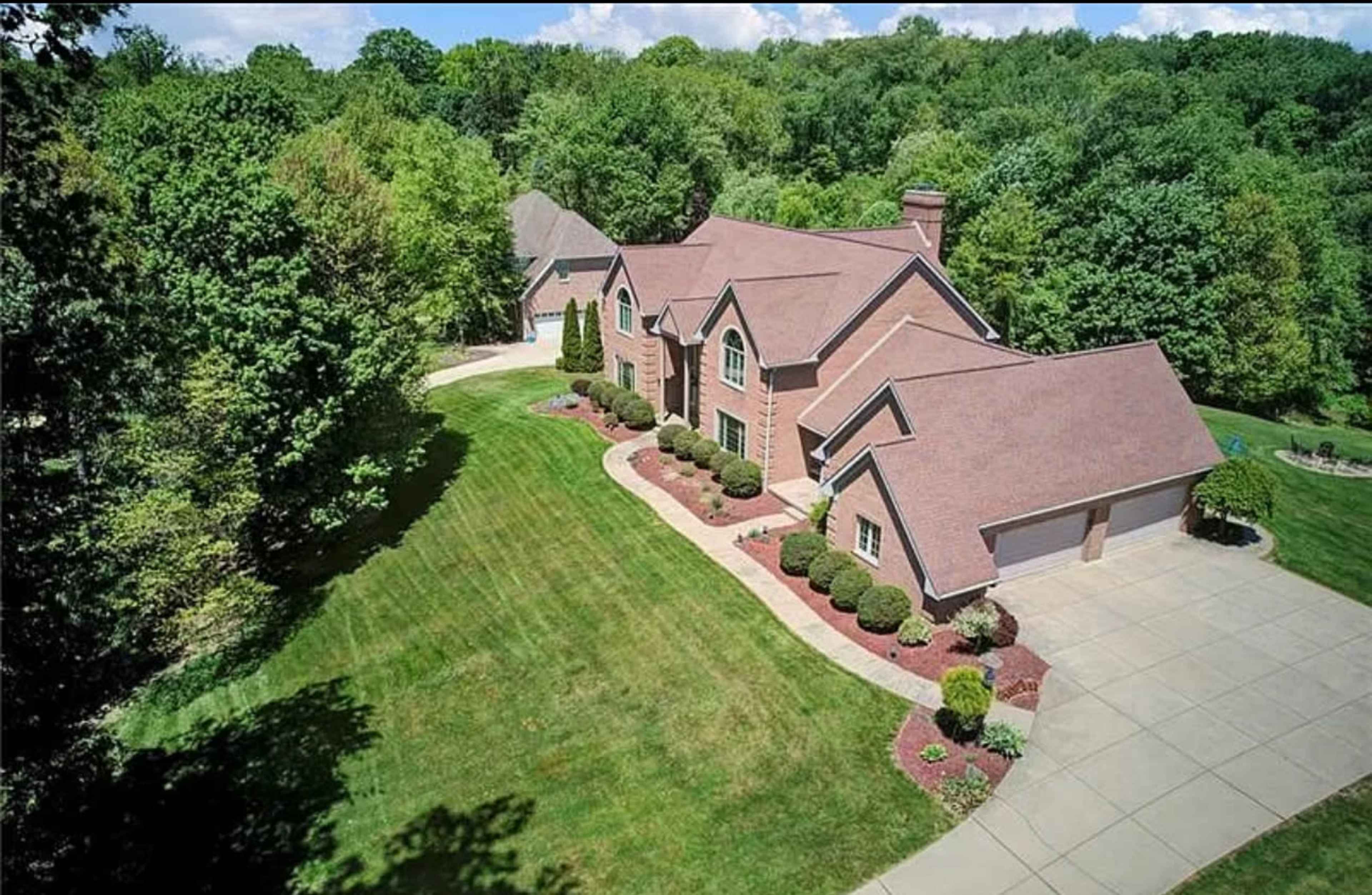 The image shows a large, two-story brick house with a sloped roof, surrounded by manicured lawns and trees.