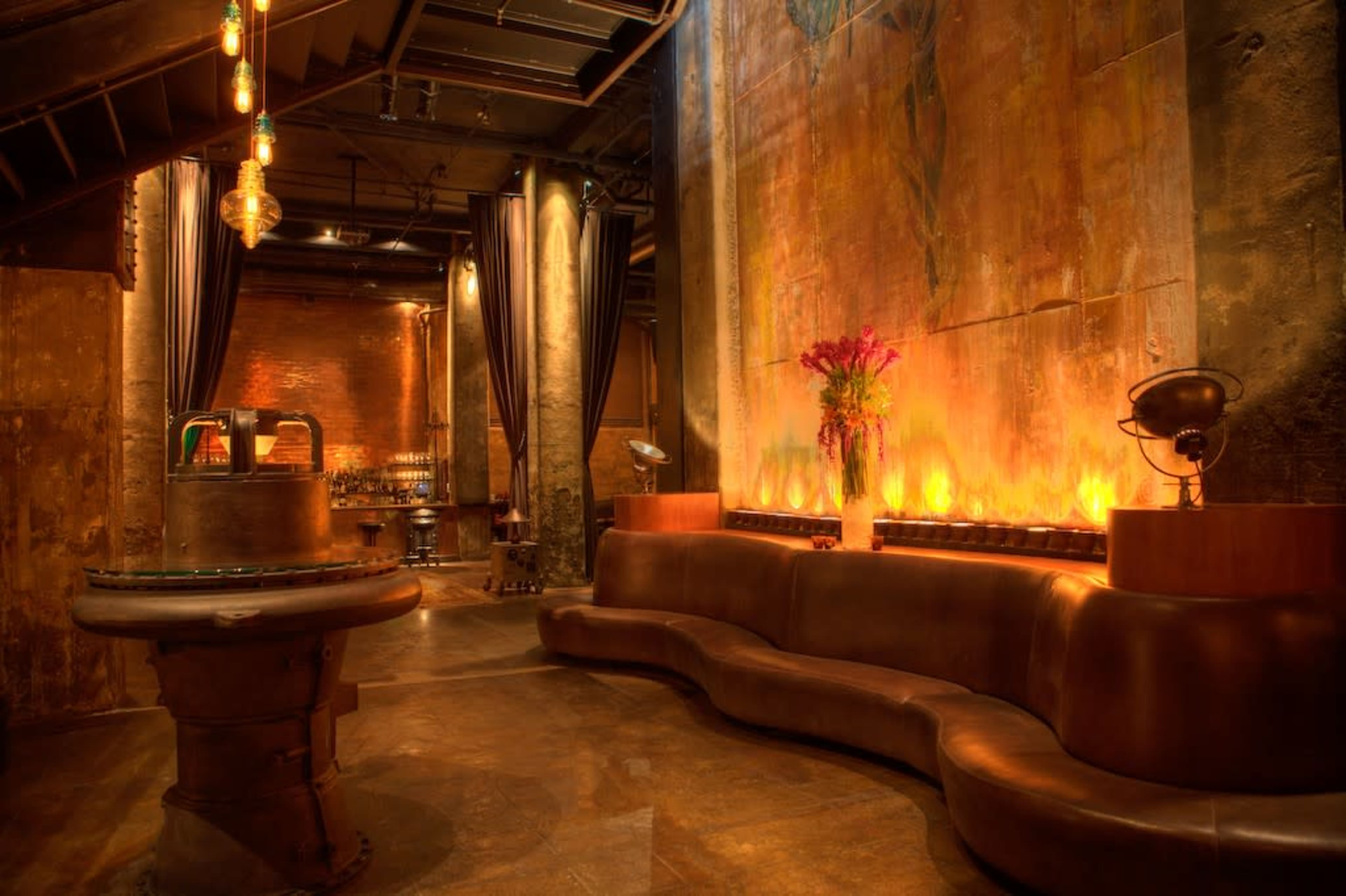 The image shows a dimly lit bar area with a curved leather sofa, large artwork on the wall, and decorative lighting fixtures.