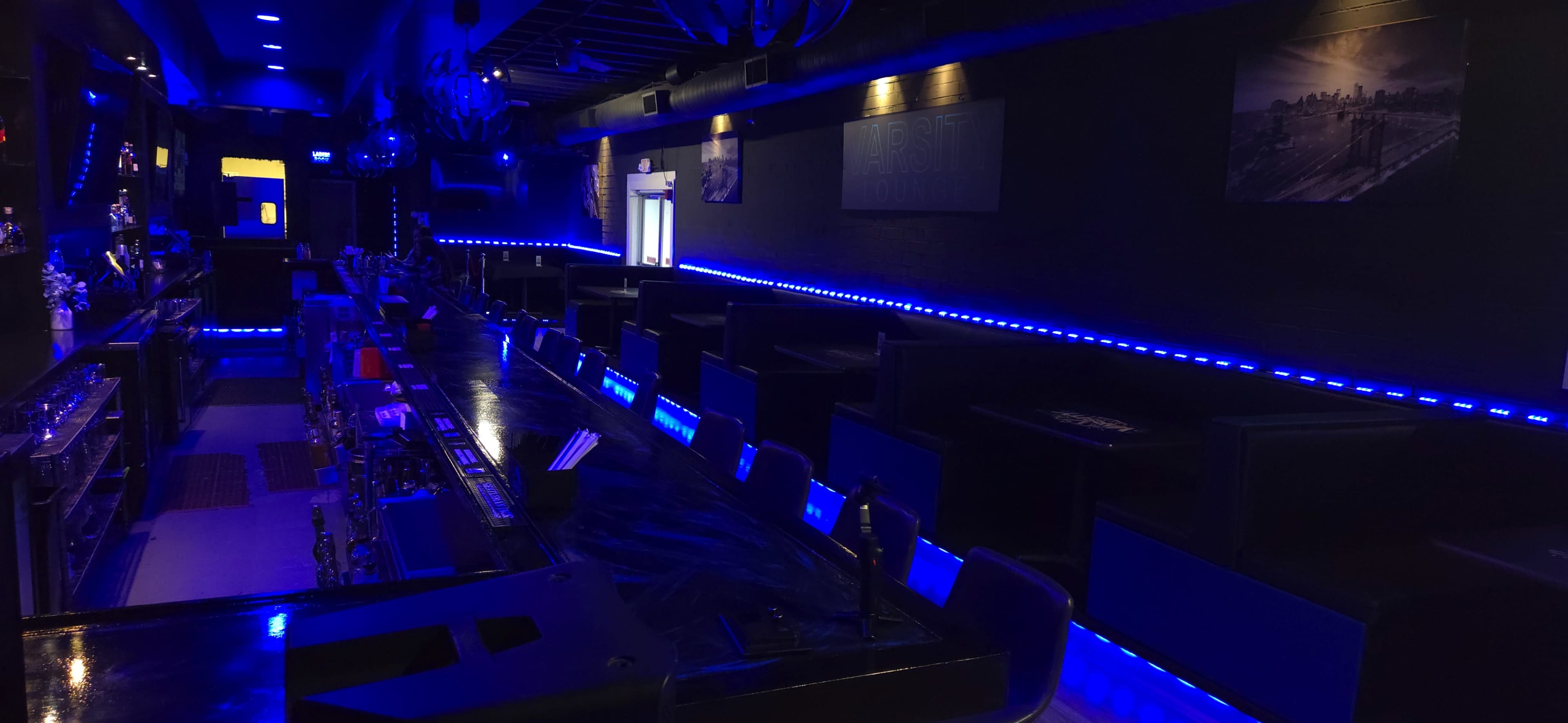 The image shows a dimly lit bar area with blue LED lights highlighting black seating and a polished counter.