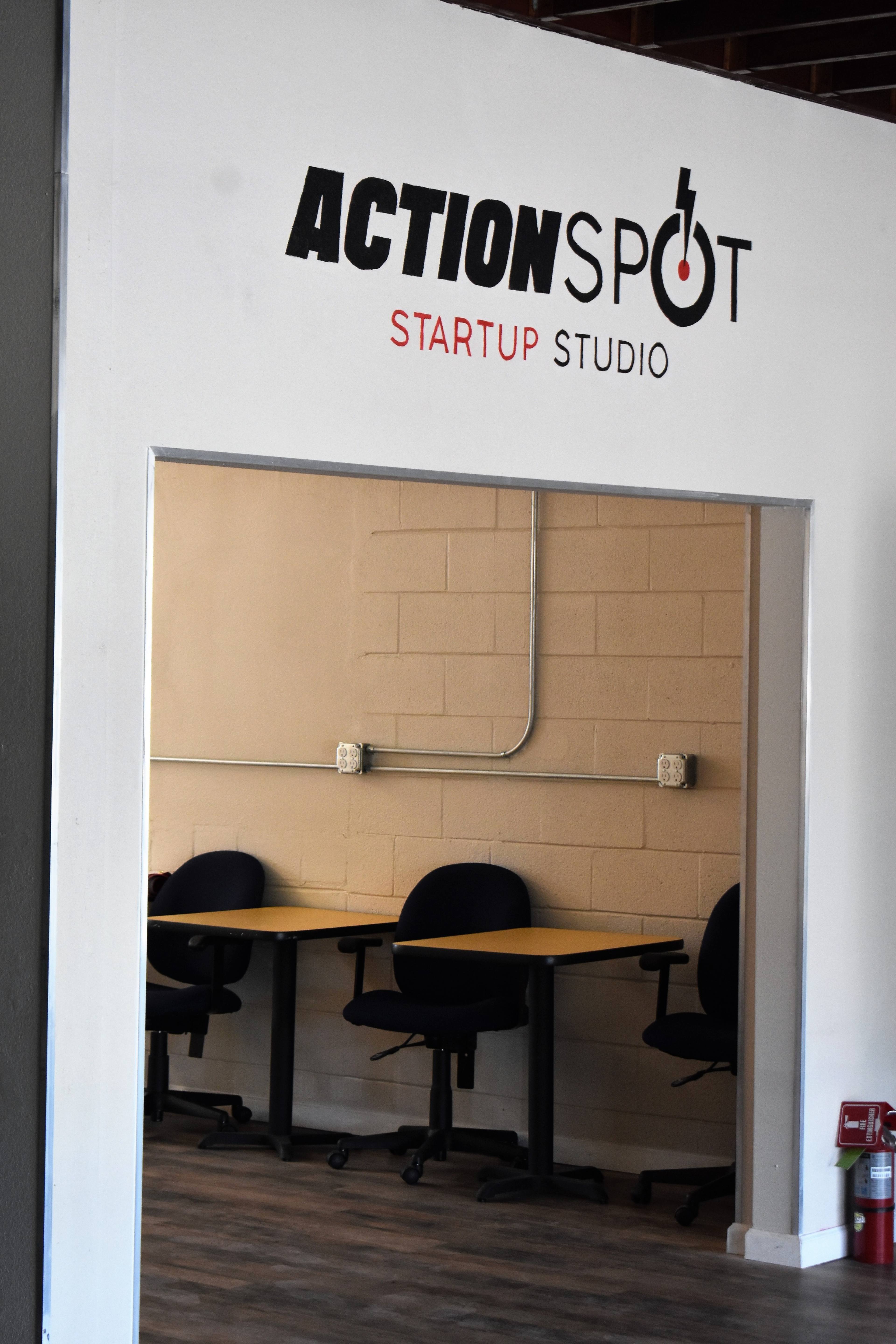 An entrance to a workspace labeled "ACTIONSPOT STARTUP STUDIO" with empty desks and chairs visible inside.