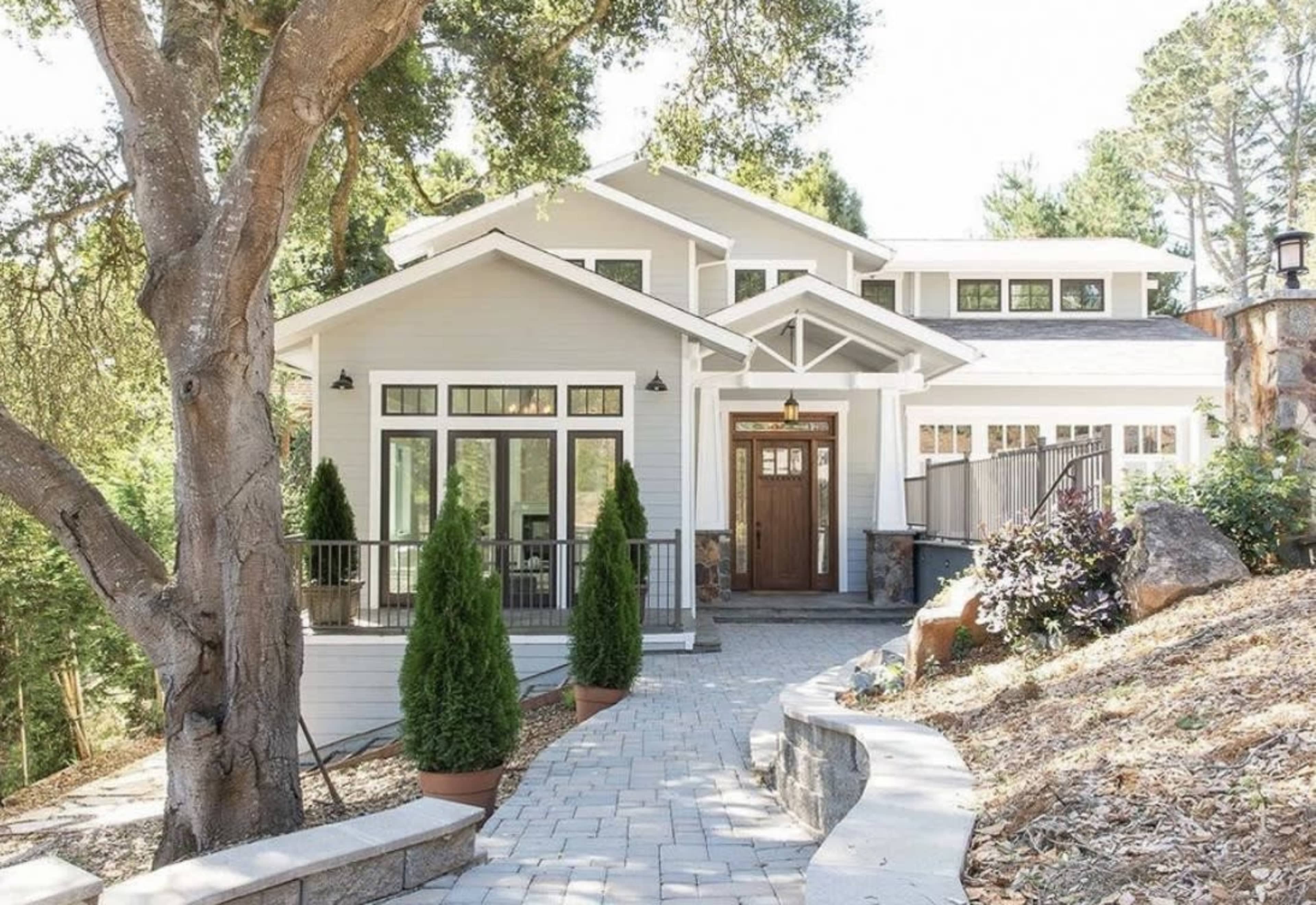 A modern two-story house with a wooden front door is surrounded by greenery and features landscaped pathways and planters.