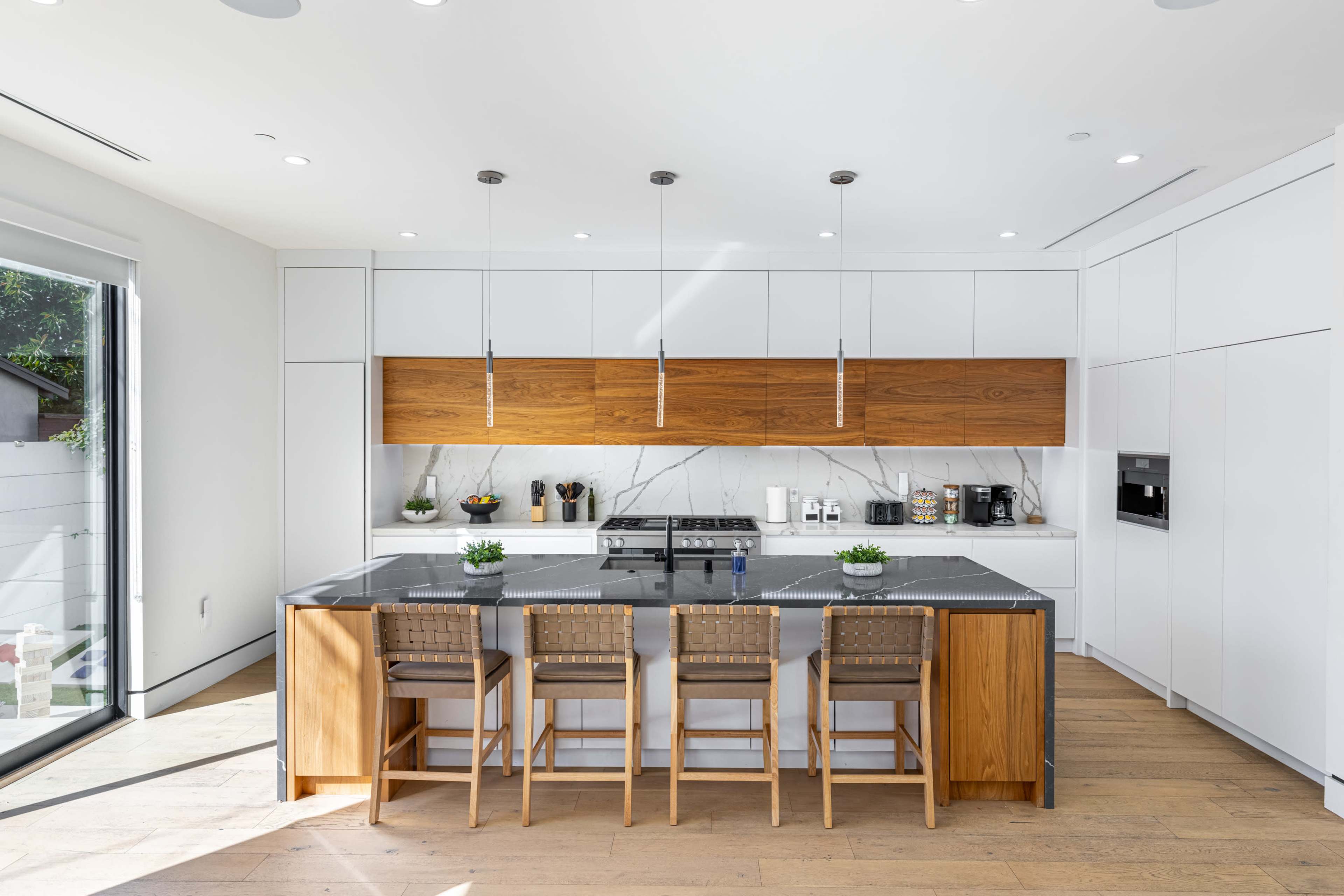 A modern kitchen featuring a large island with four bar stools, sleek cabinetry, and a gas stove under pendant lights.