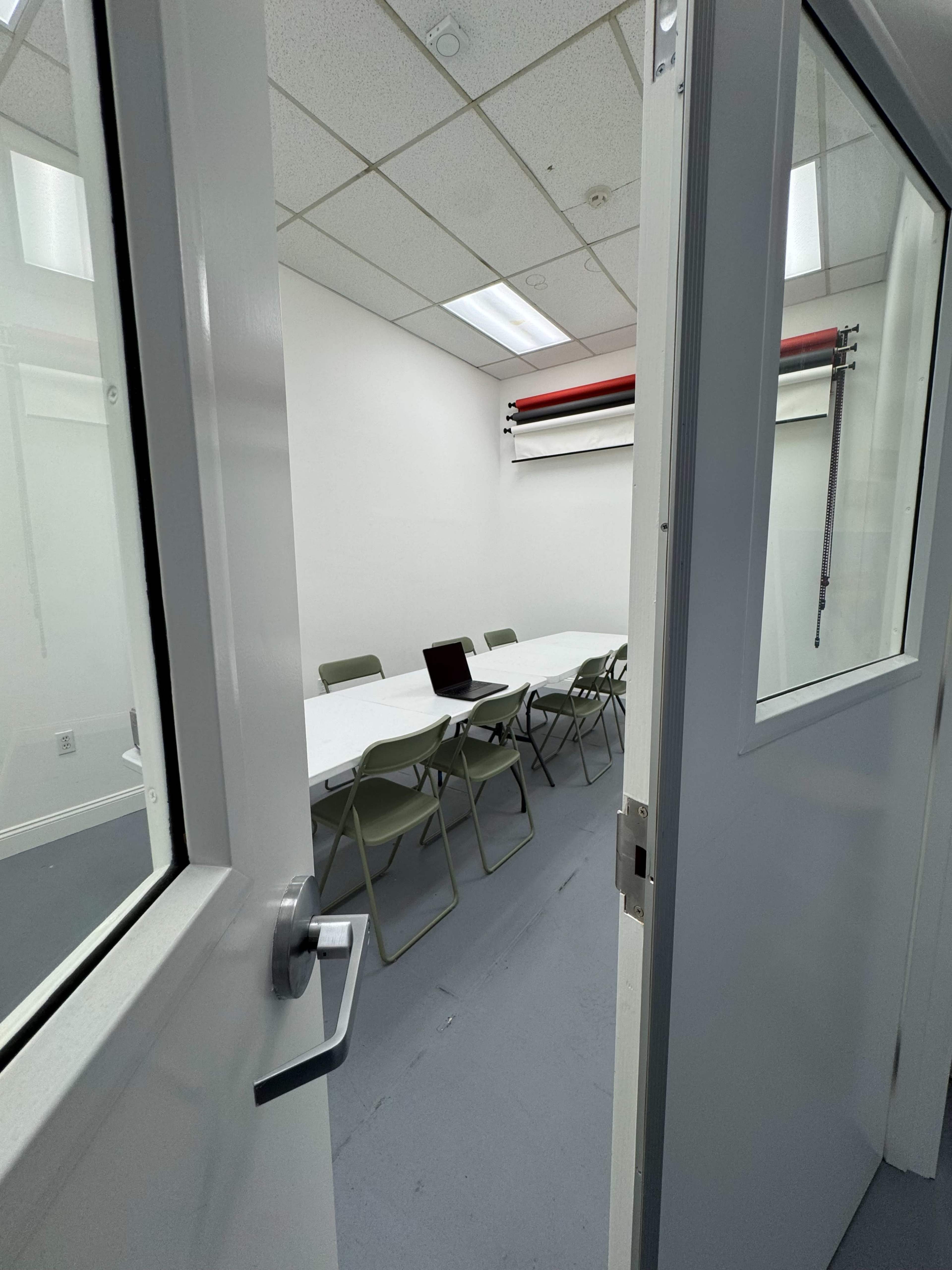 A conference room with a large table surrounded by chairs and a laptop on the table, viewed through an open door.