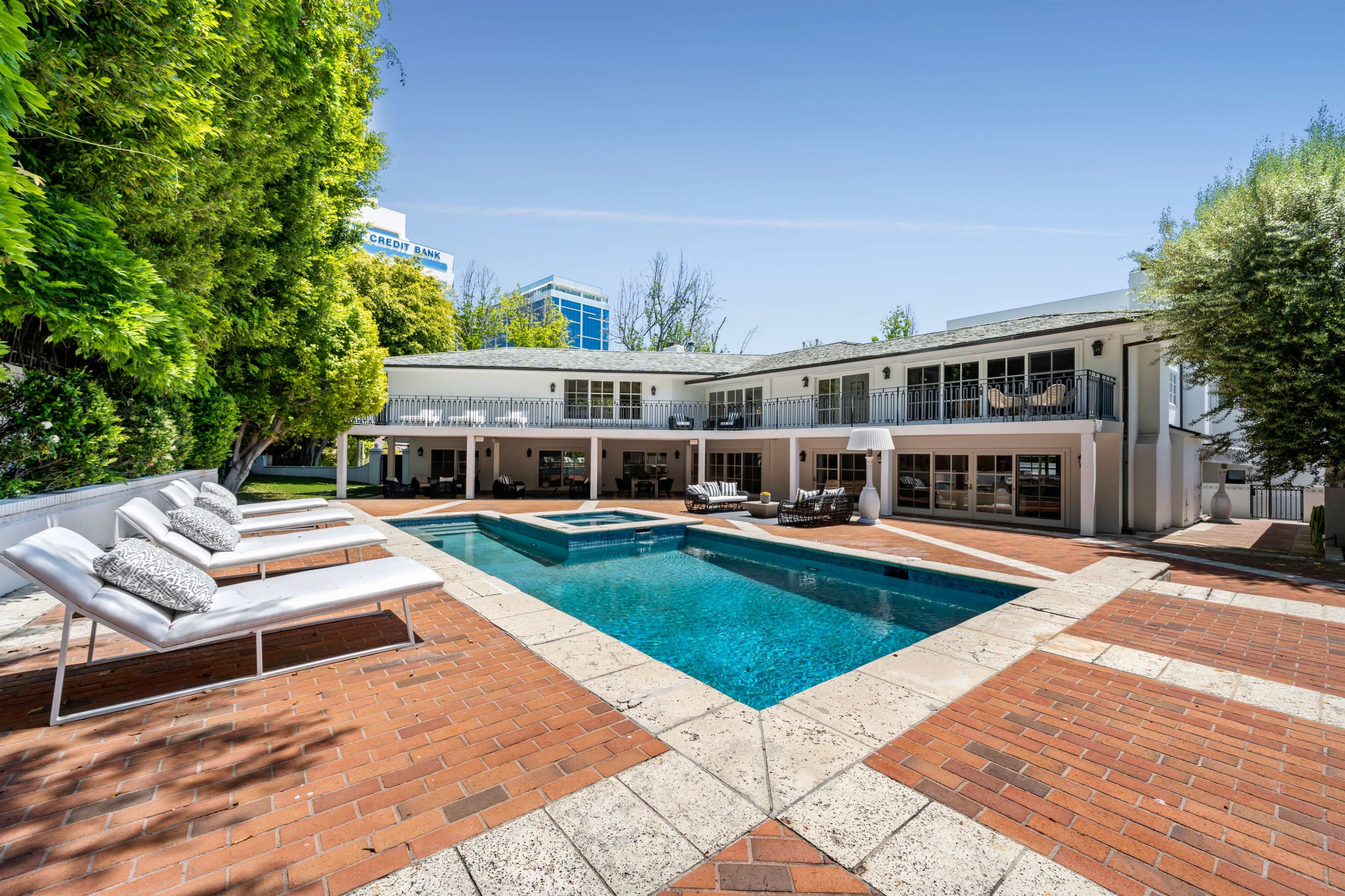 A modern two-story house with a swimming pool and lounge chairs set in a landscaped outdoor area.