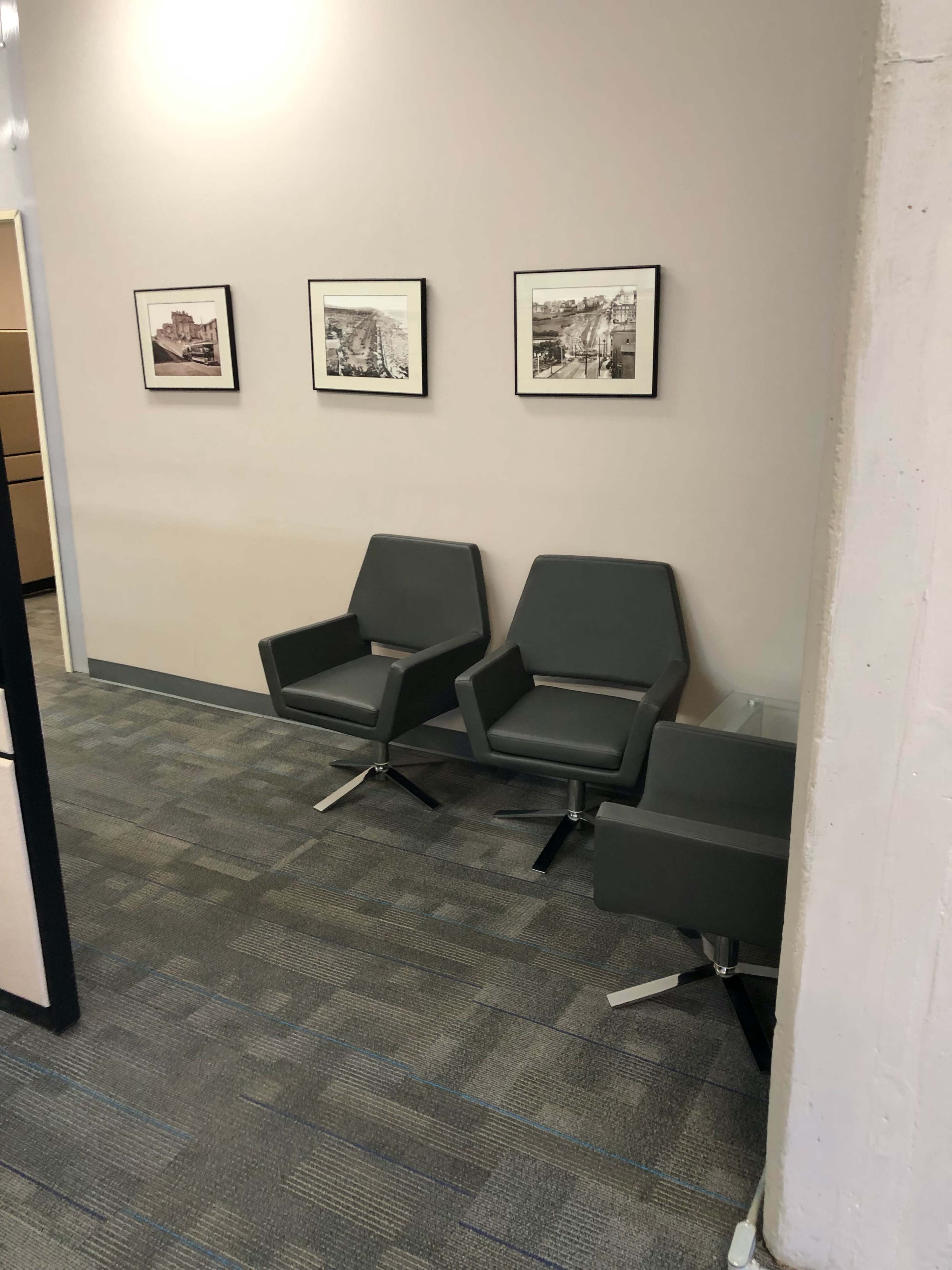 A hallway with gray walls, two modern gray chairs, and framed black-and-white photographs on the wall.