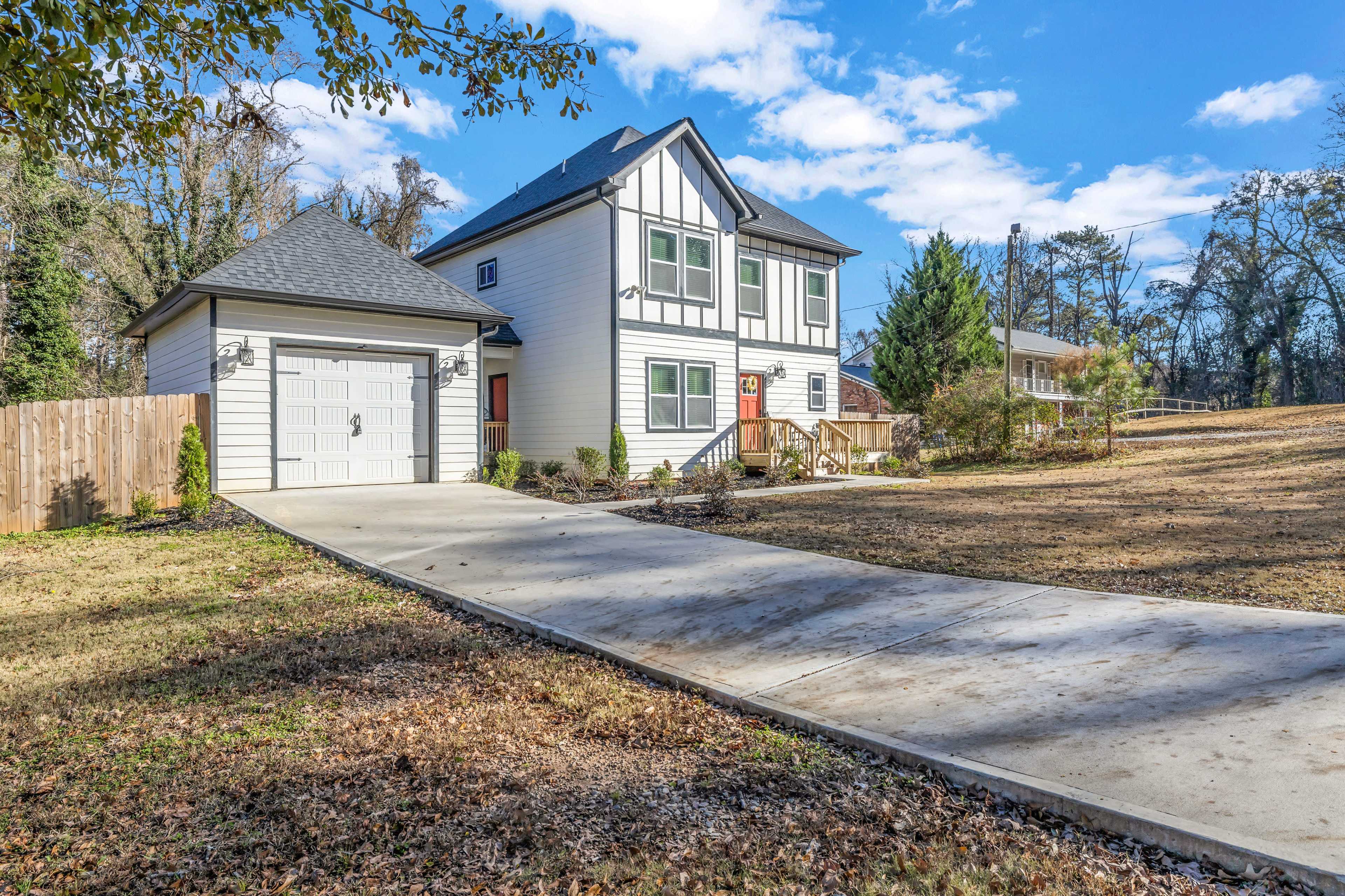A two-story house with a garage sits on a spacious lot, featuring a well-maintained driveway and surrounded by grass and trees.