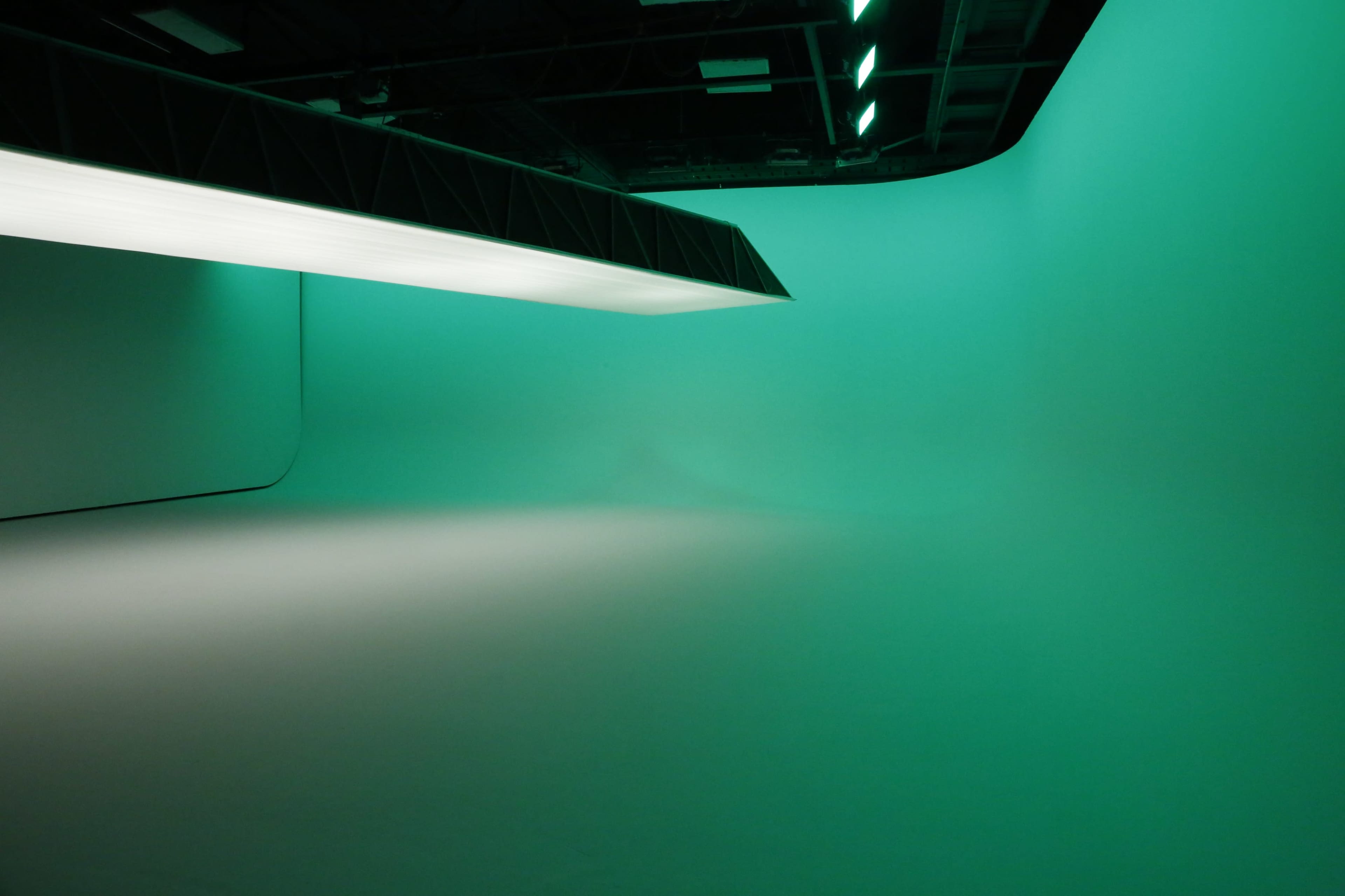 An empty studio space with a smooth, gradient backdrop illuminated in green.