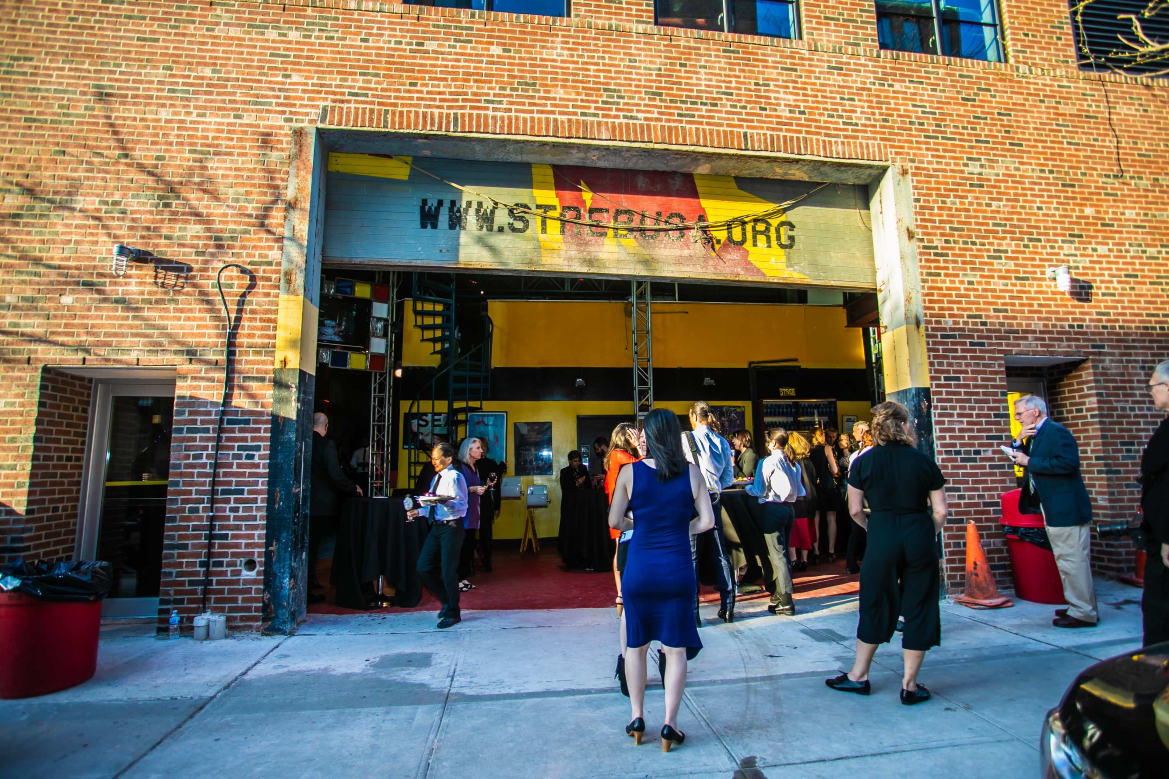 A crowd of people gathers outside a brick building with an open entrance displaying the website URL "www.street.org."
