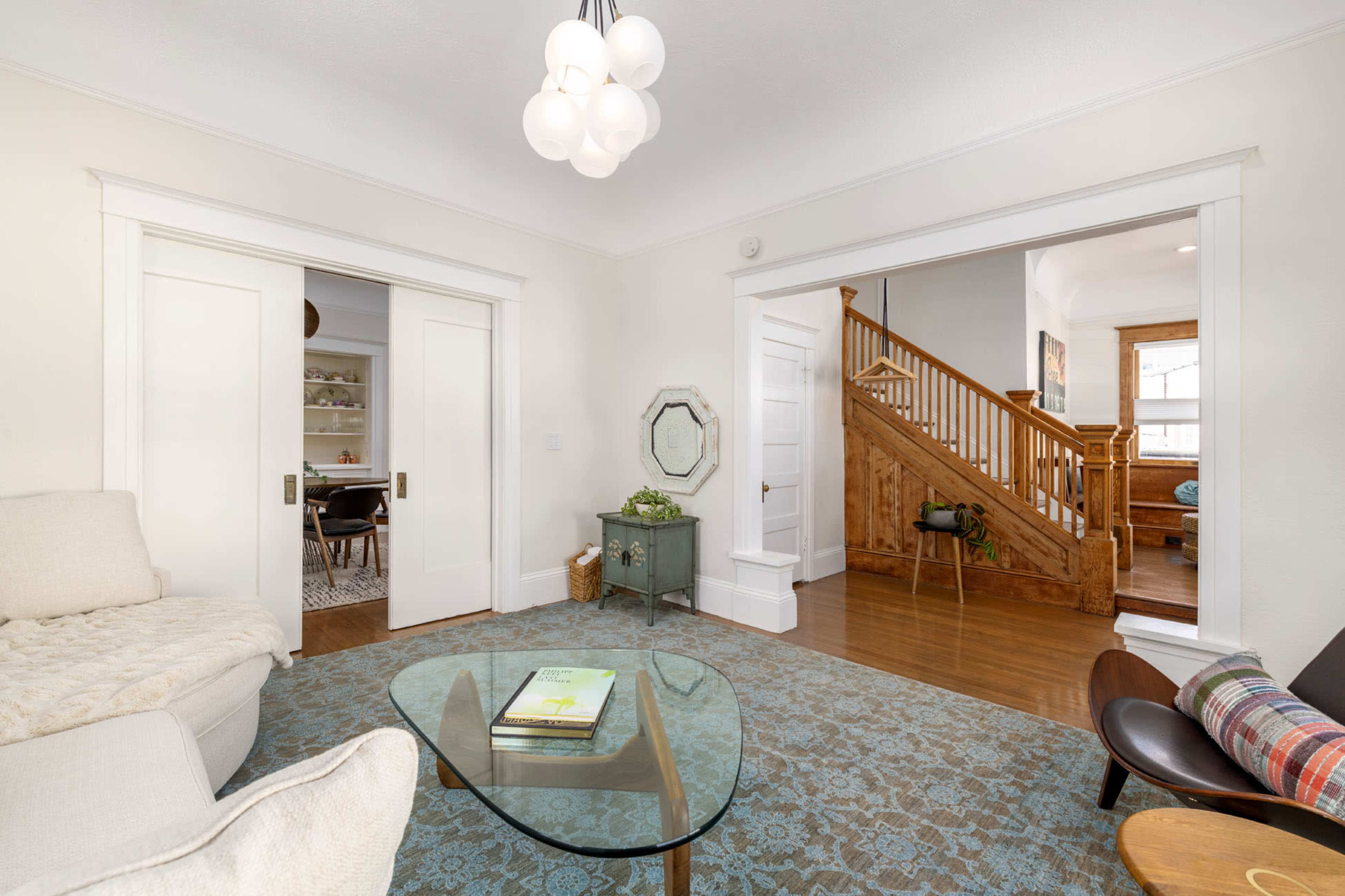 A cozy living room with a light-colored sofa, a glass coffee table, and a view of a staircase leading to an upper floor.
