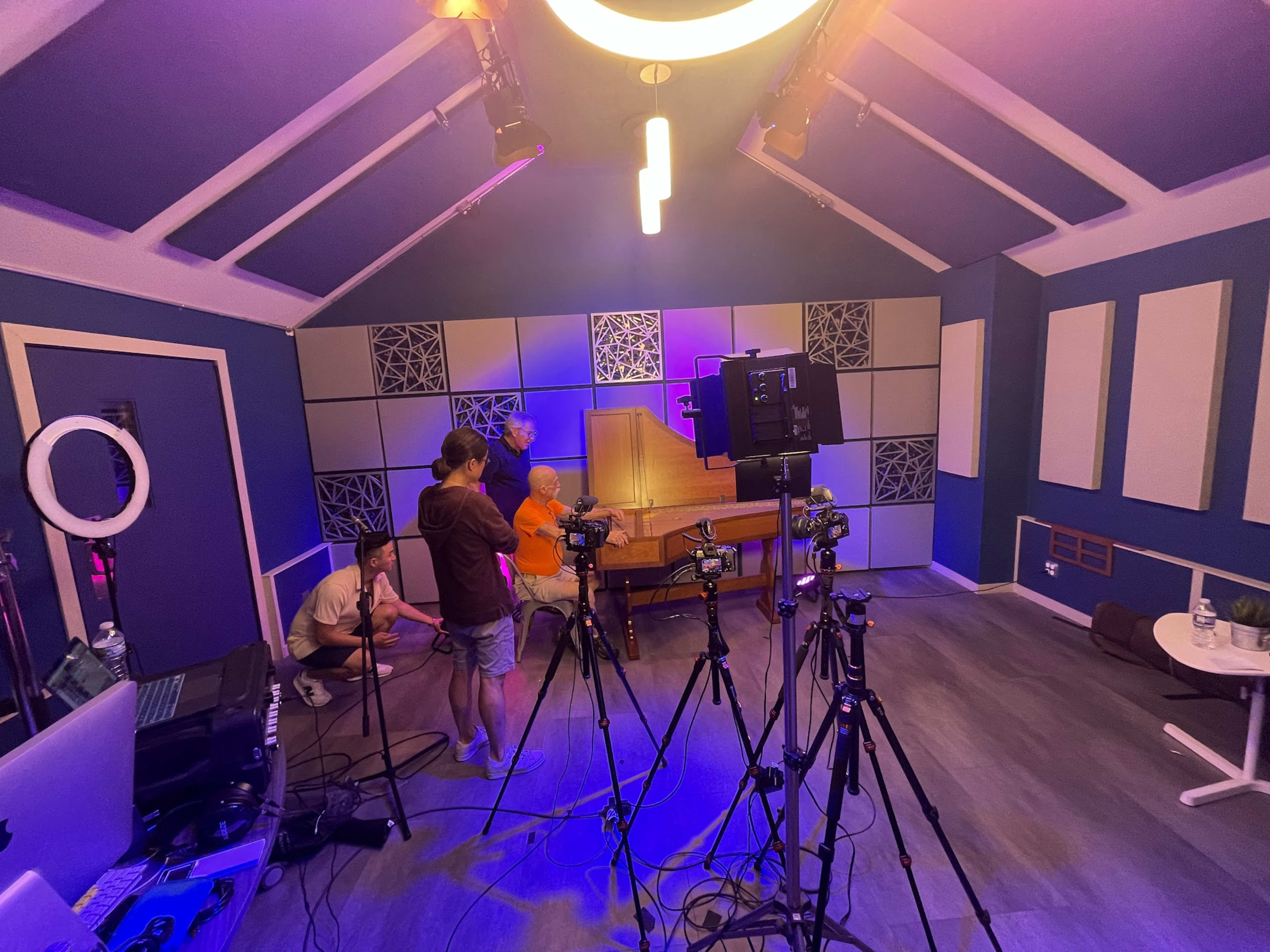 A group of people prepares for a shoot in a studio equipped with multiple cameras and colorful lighting.