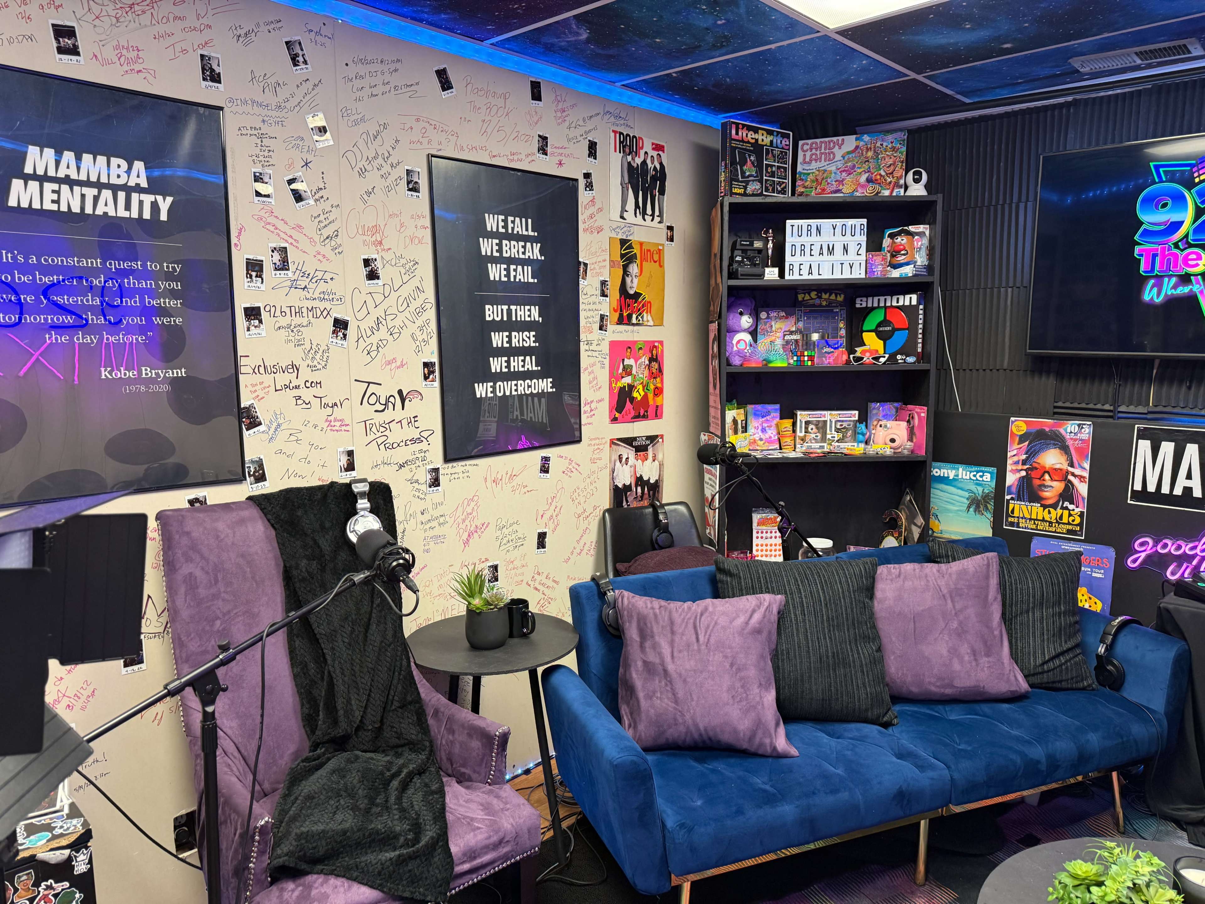 The image shows a vibrant studio or creative space featuring purple couches, motivational quotes on the walls, and various colorful decorations and memorabilia.