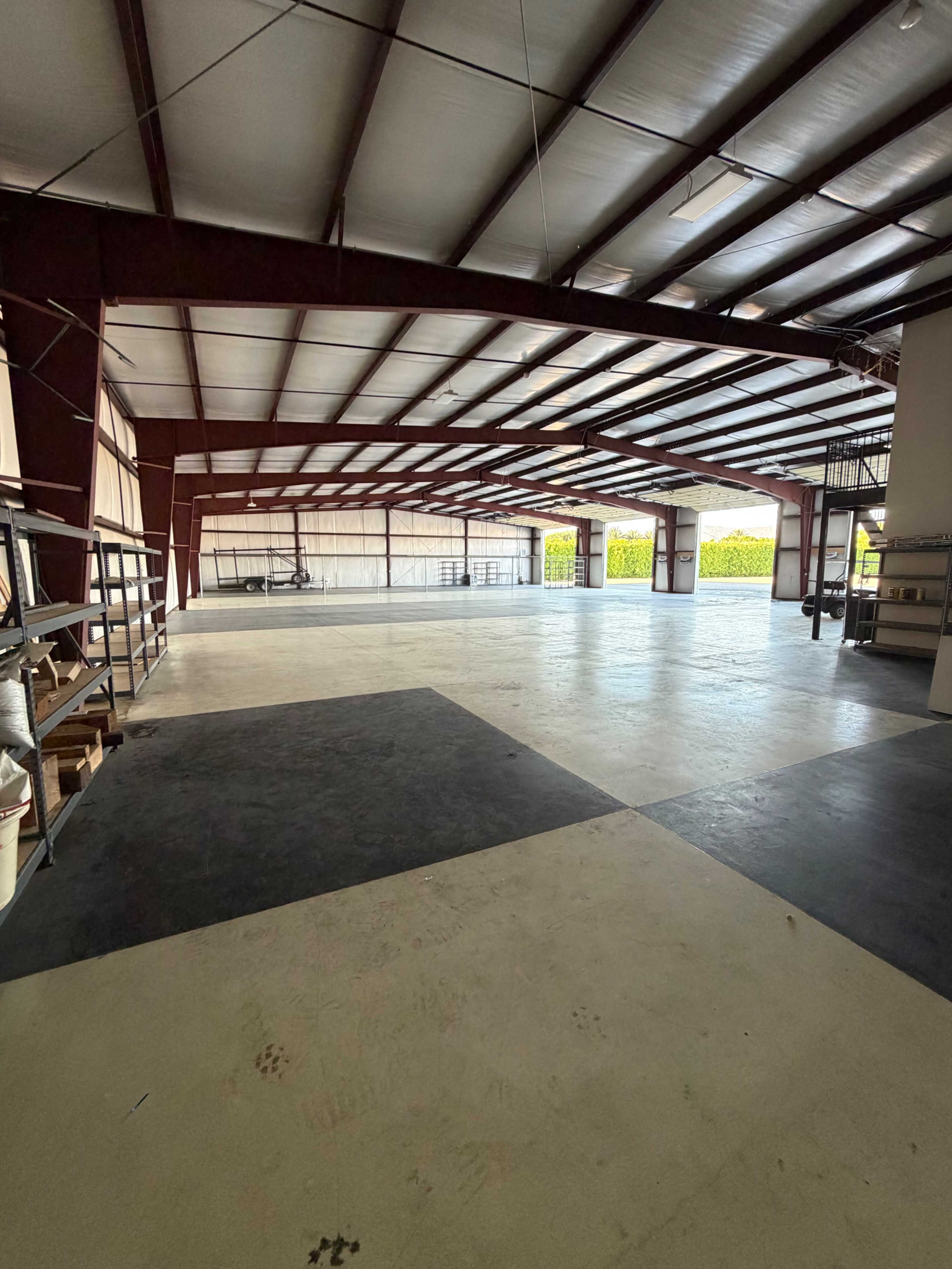 The image shows a spacious, open warehouse with metal beams and a concrete floor.