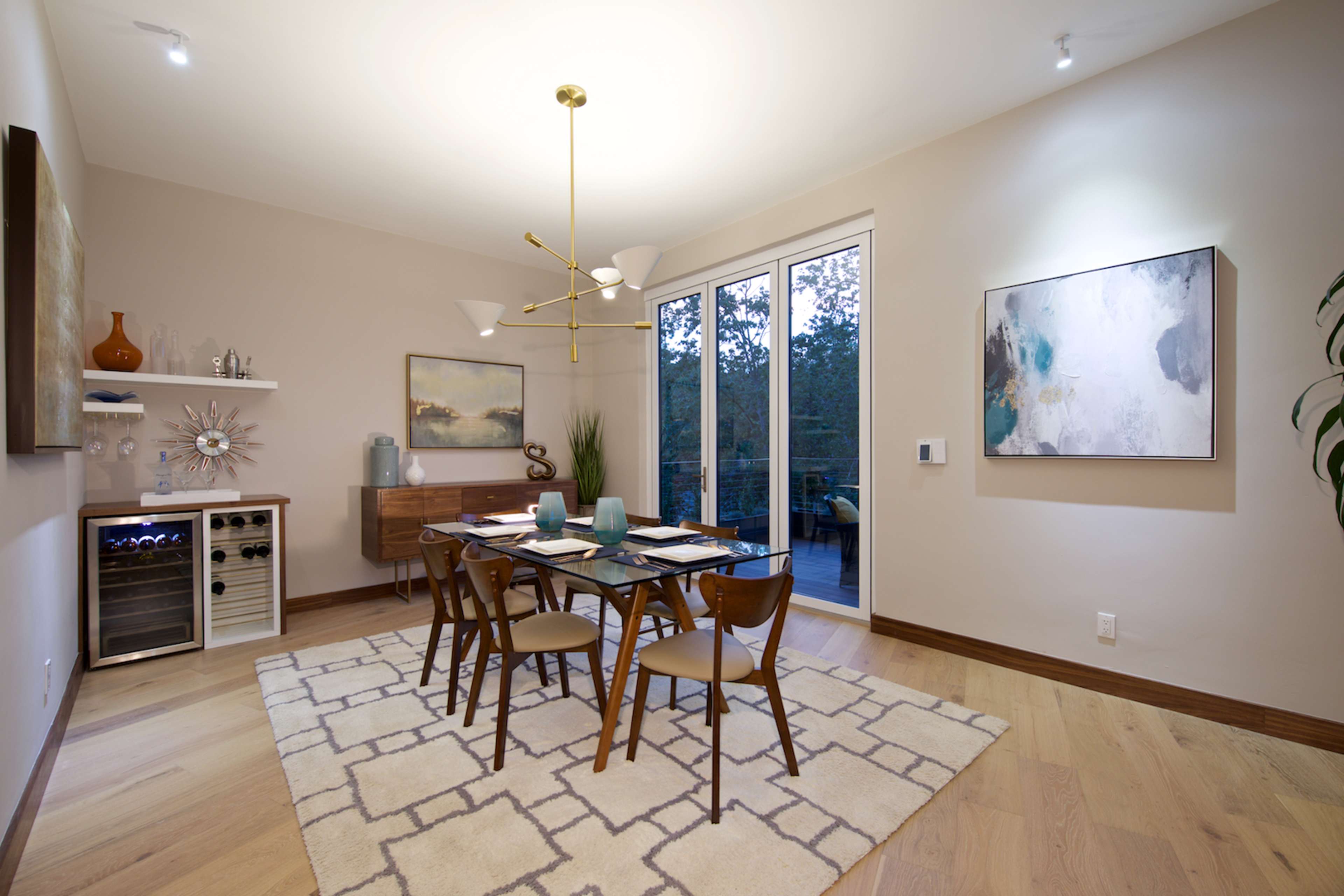 A modern dining area features a table with chairs, a sideboard, and large windows overlooking greenery.