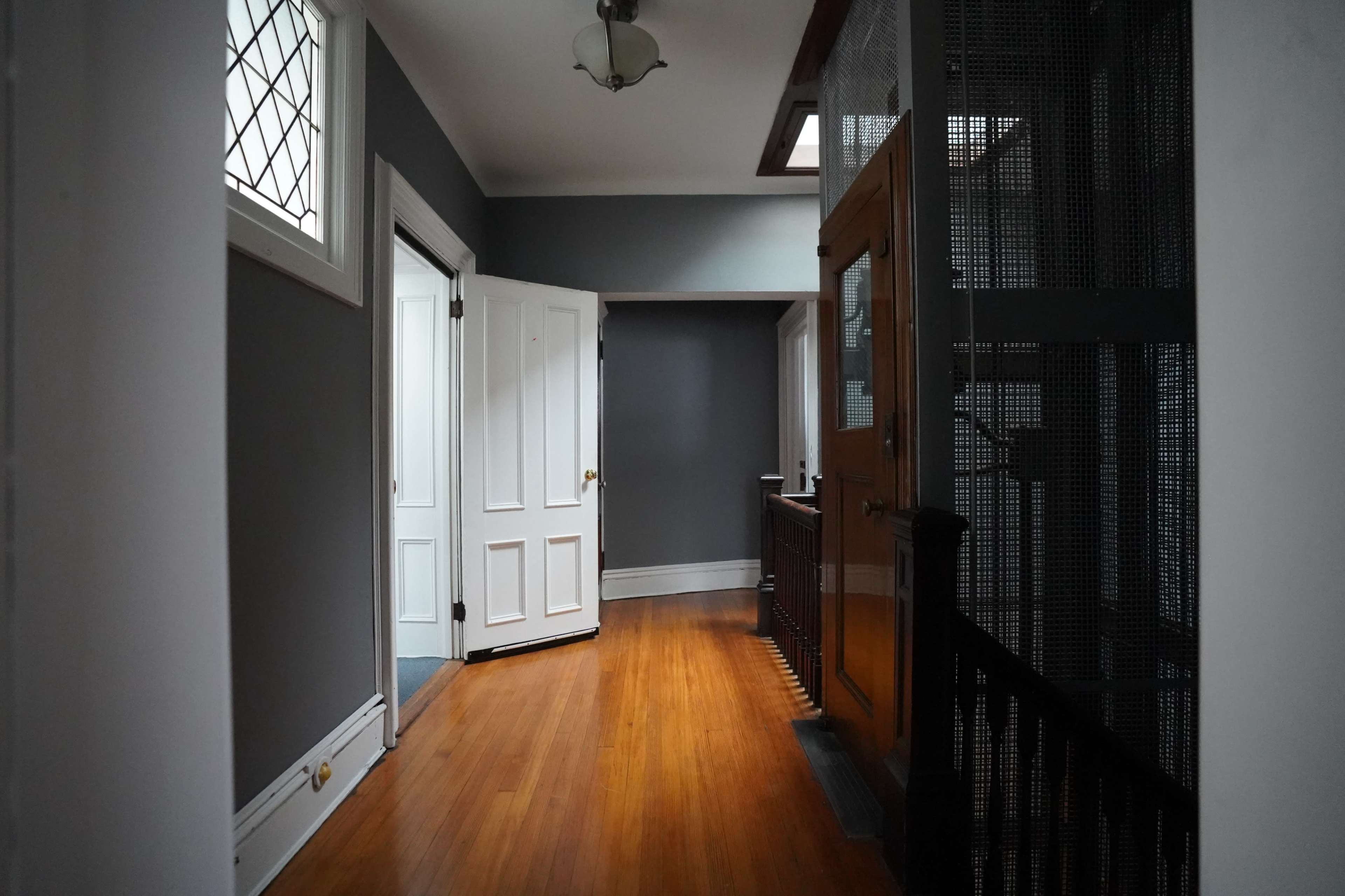 A corridor with wooden floors, gray walls, and multiple doors leading to different rooms.