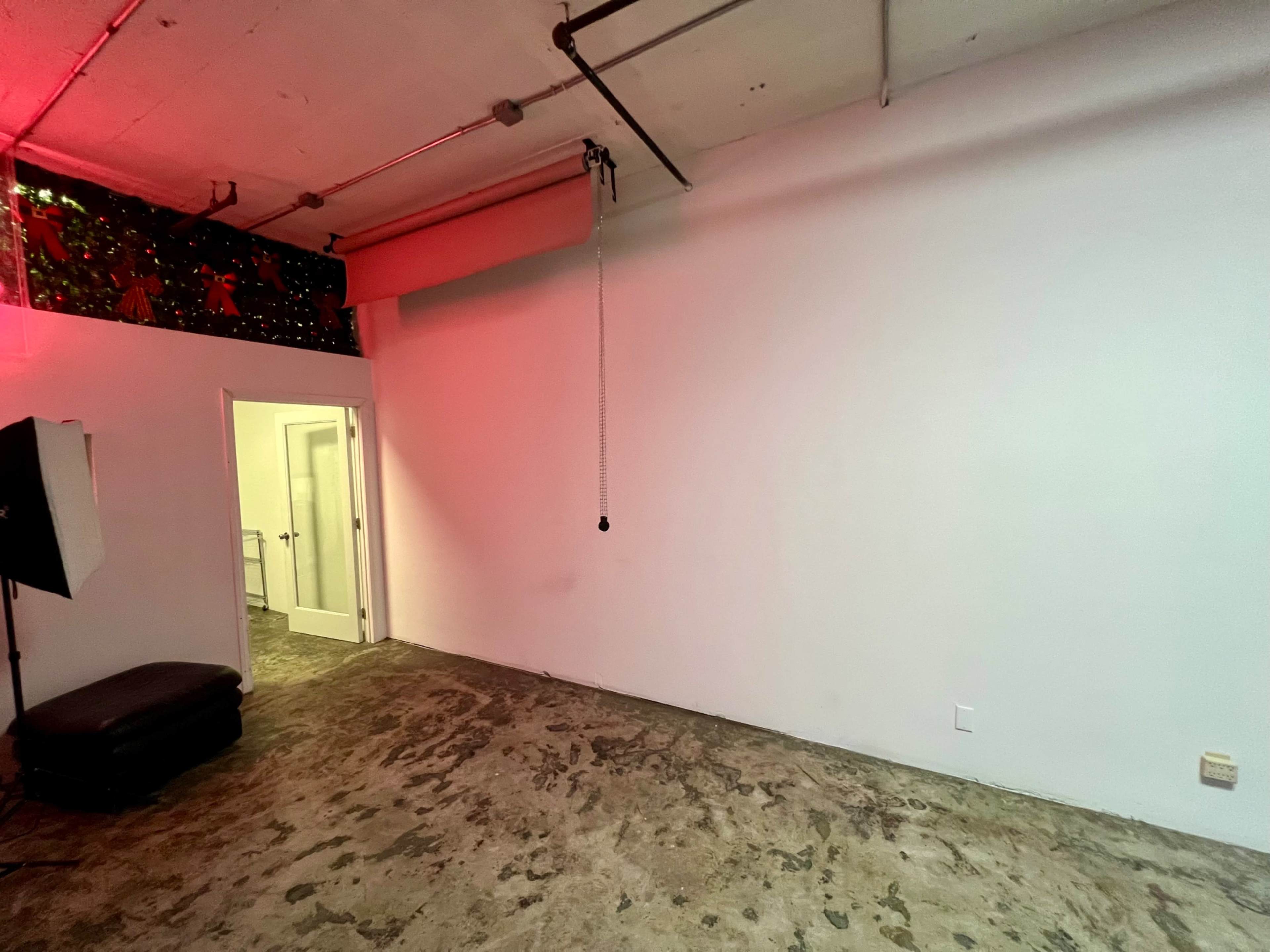 The image shows an empty room with a concrete floor, a white wall, and a partially visible doorway leading to another space.